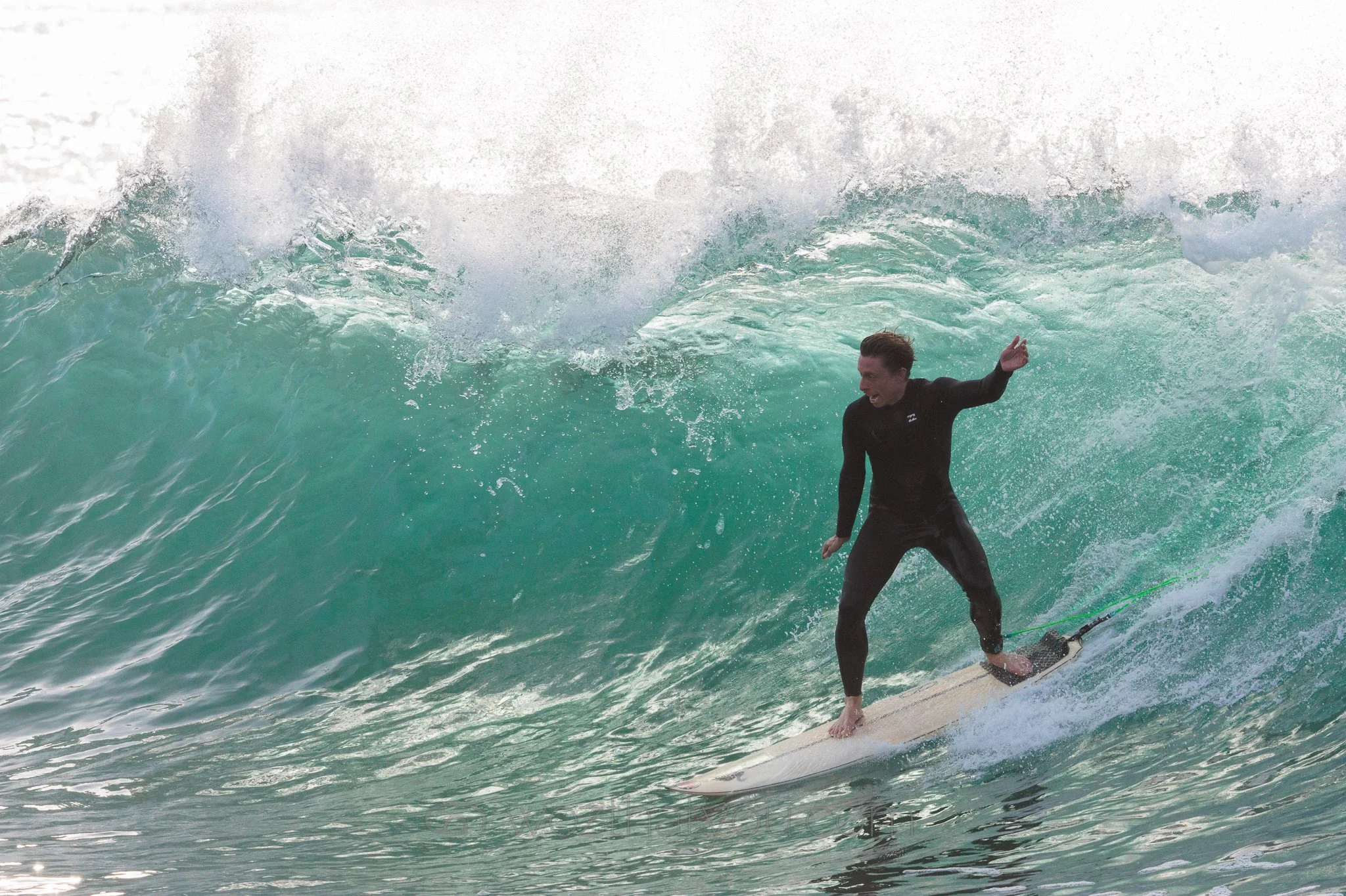 Person surfing on a large wave in the ocean, wearing a wetsuit and holding a surfboard.