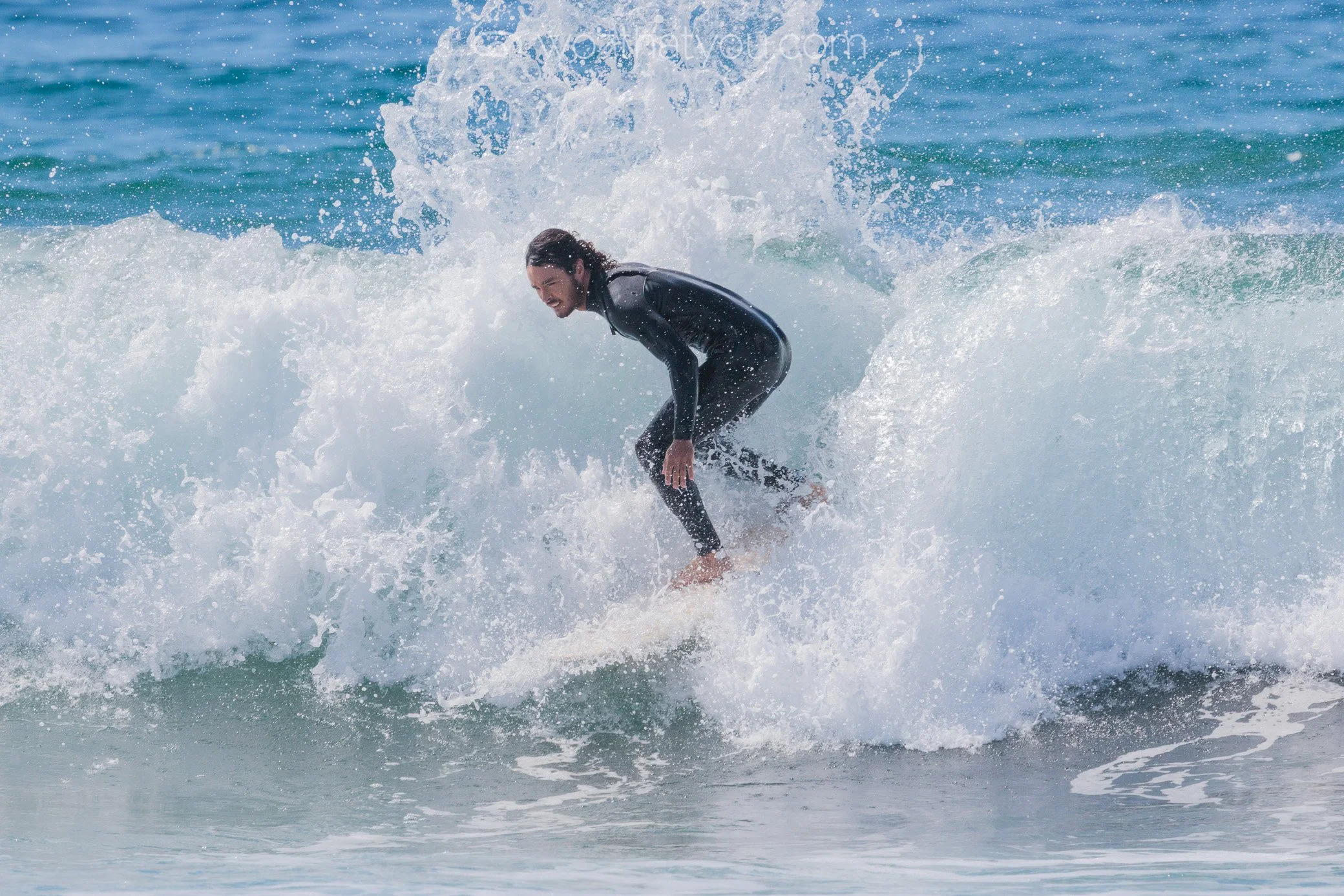 A person surfing on a wave in the ocean, wearing a black wetsuit.