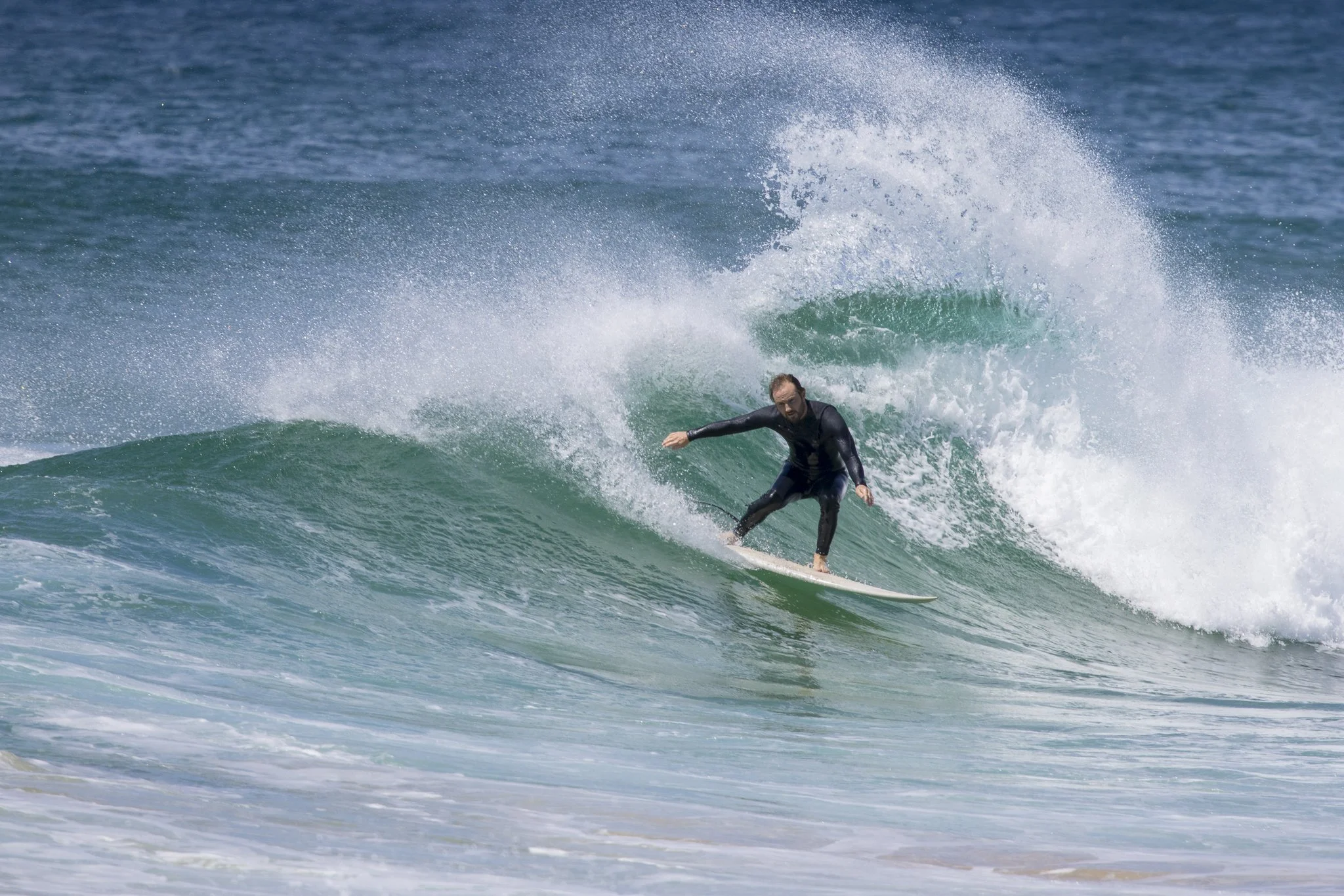 A man in a black wetsuit surfing a wave in the ocean.