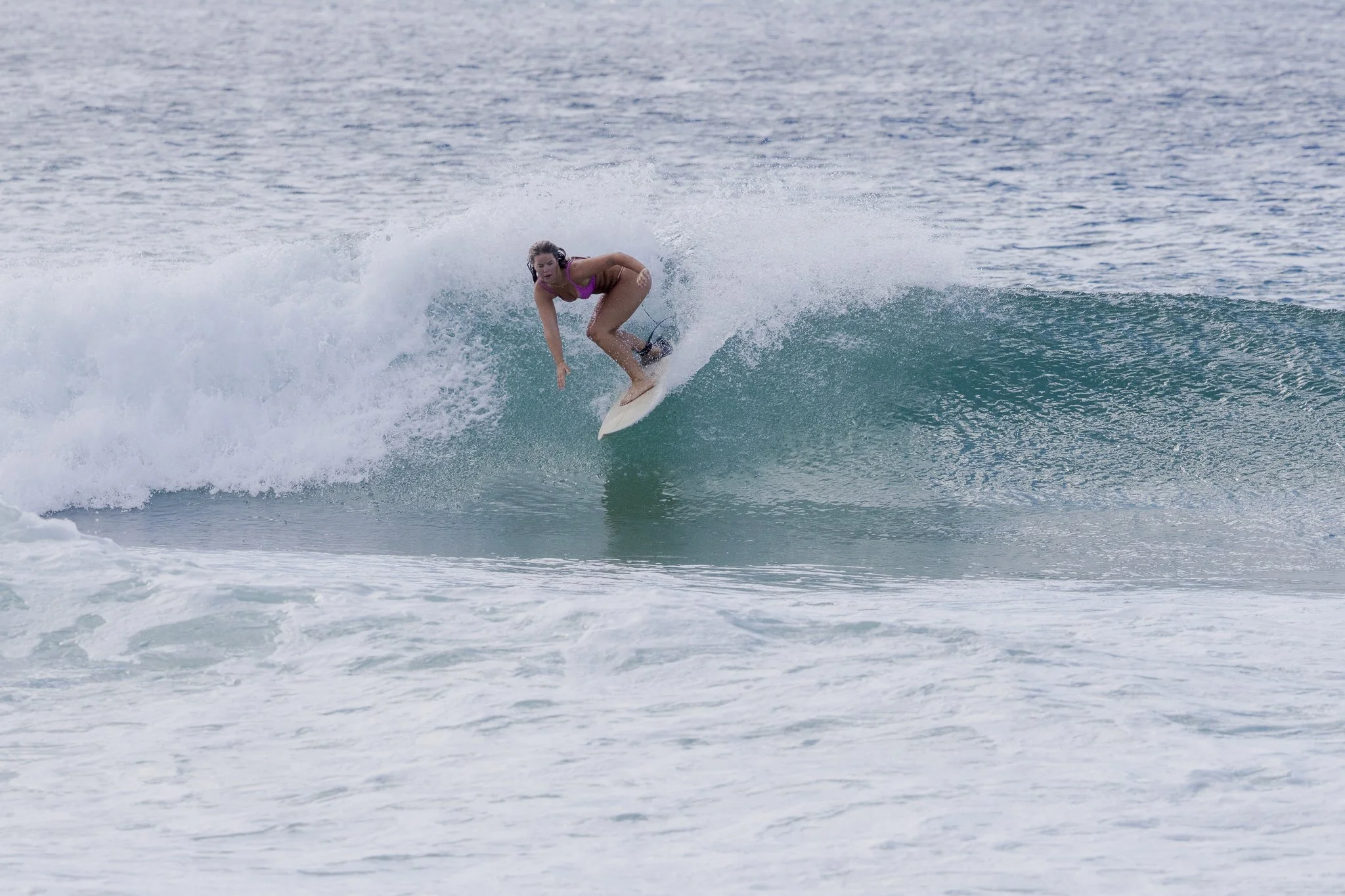A woman surfing on a small wave in the ocean, wearing a pink bikini and riding a white surfboard.
