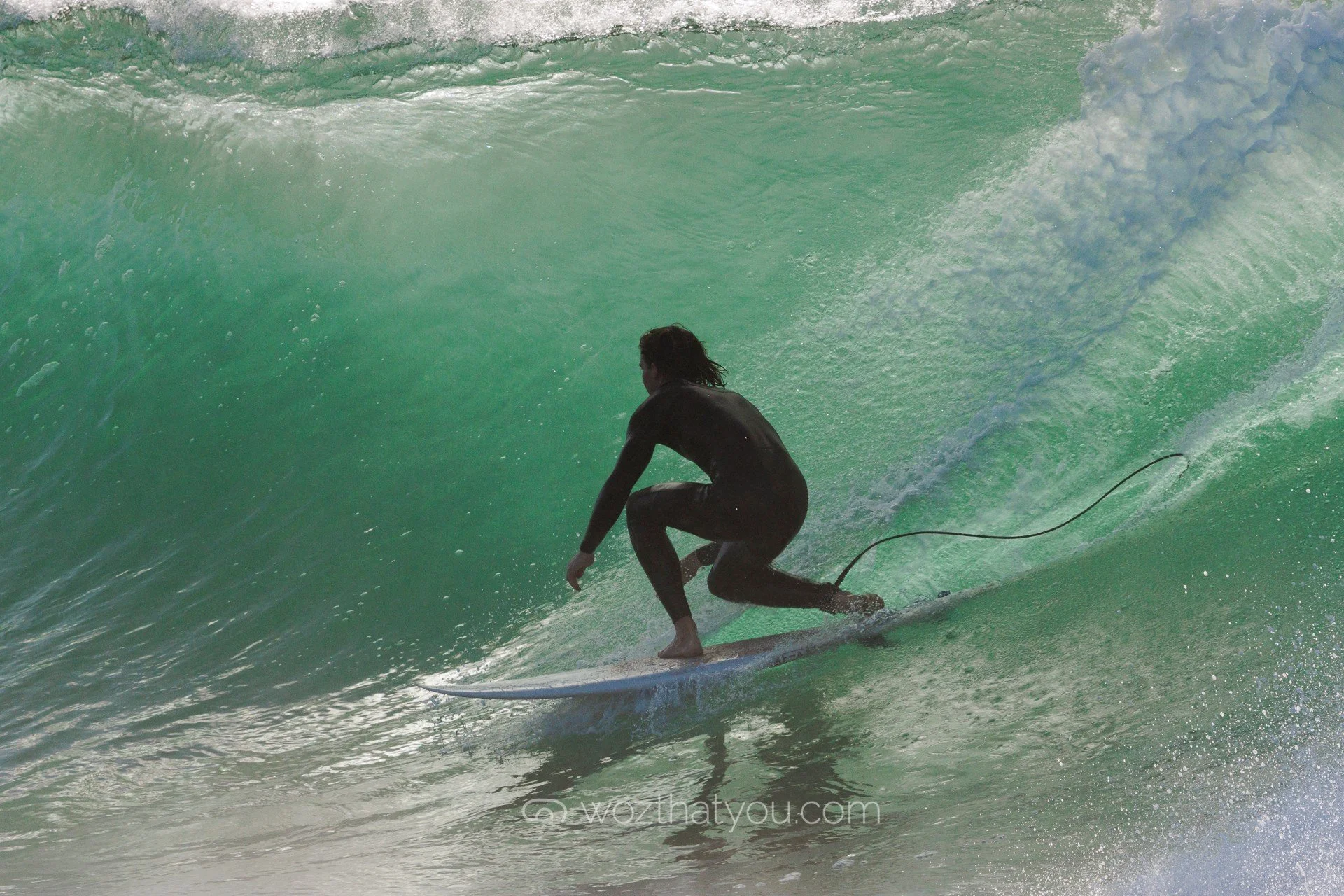 A person riding a surfboard inside a large green wave at the beach.