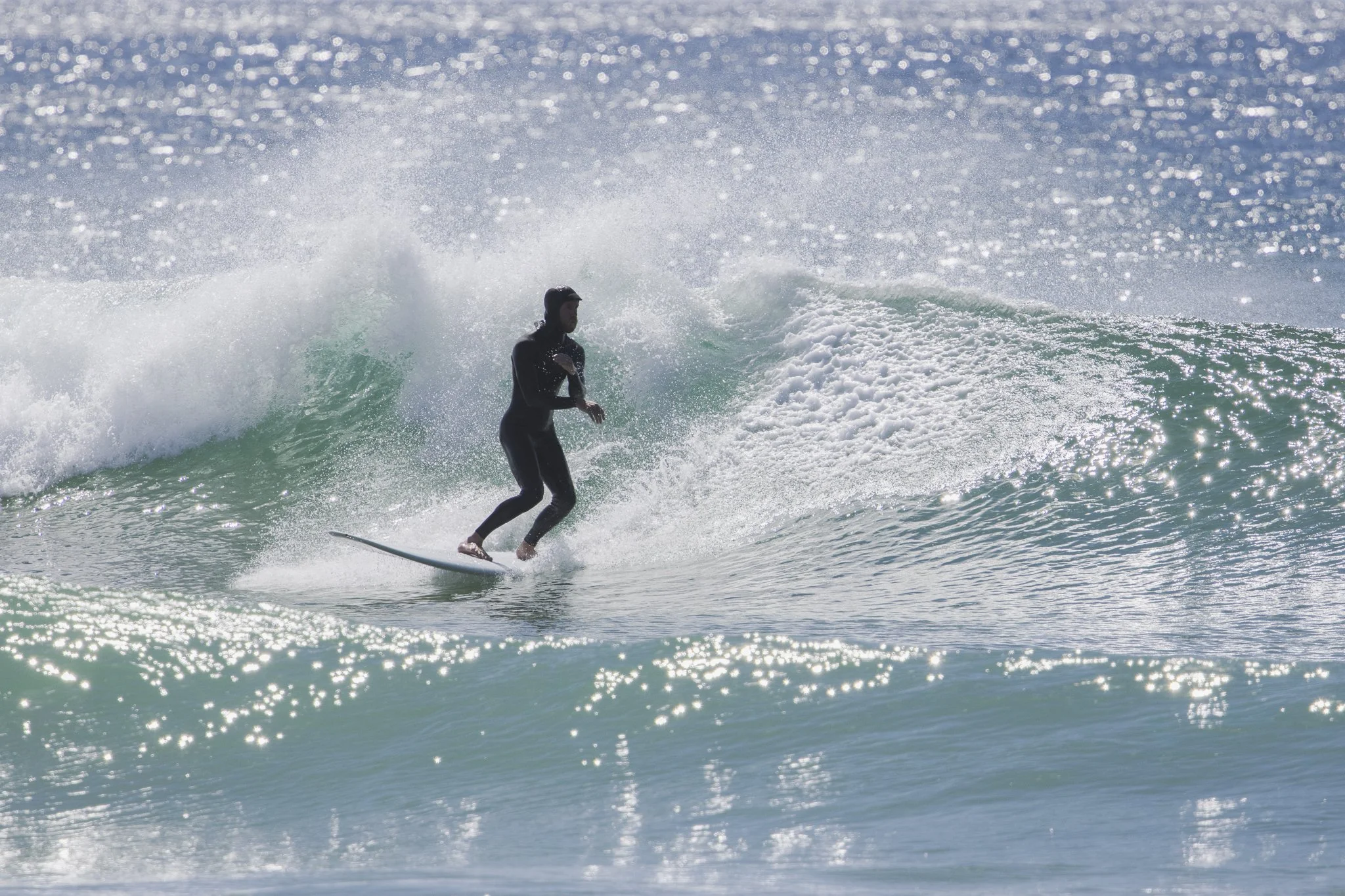 A person in a black wetsuit riding a surfboard on a wave in the ocean.