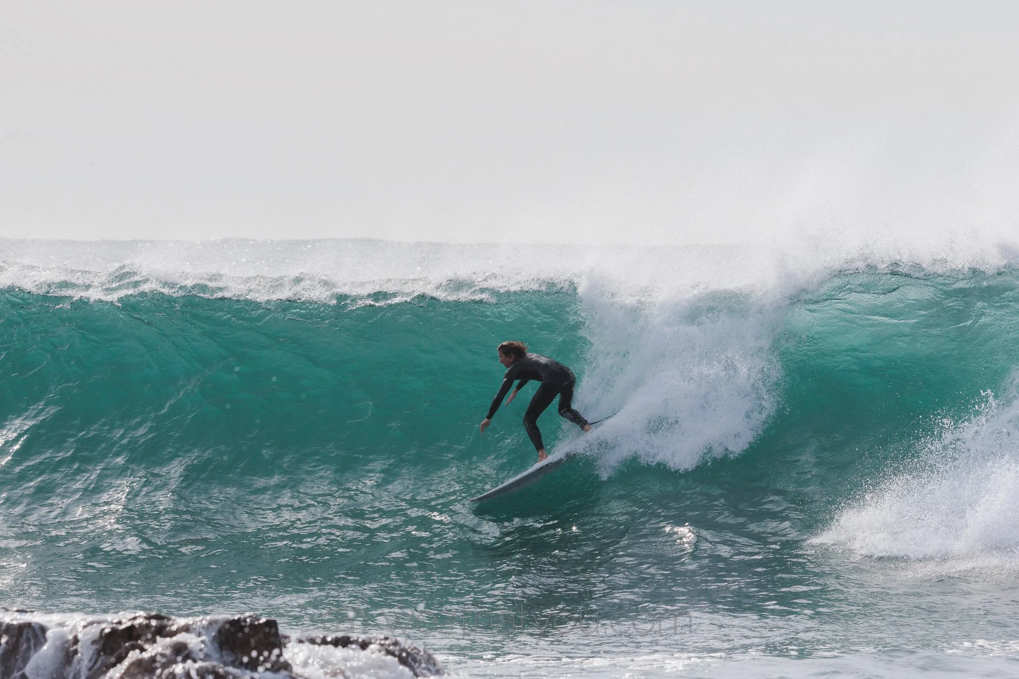A person surfing on a wave in the ocean, wearing a black wetsuit.