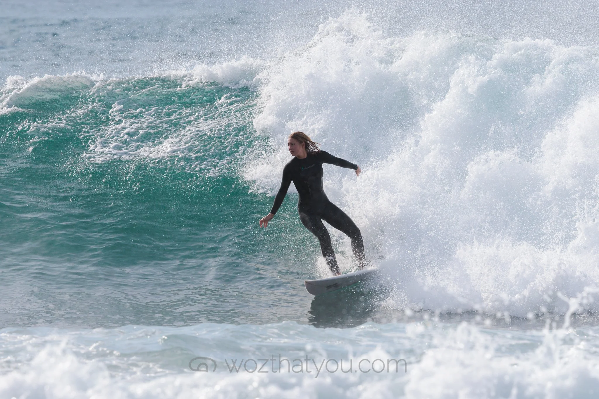 A woman in a black wetsuit surfing on a wave in the ocean.