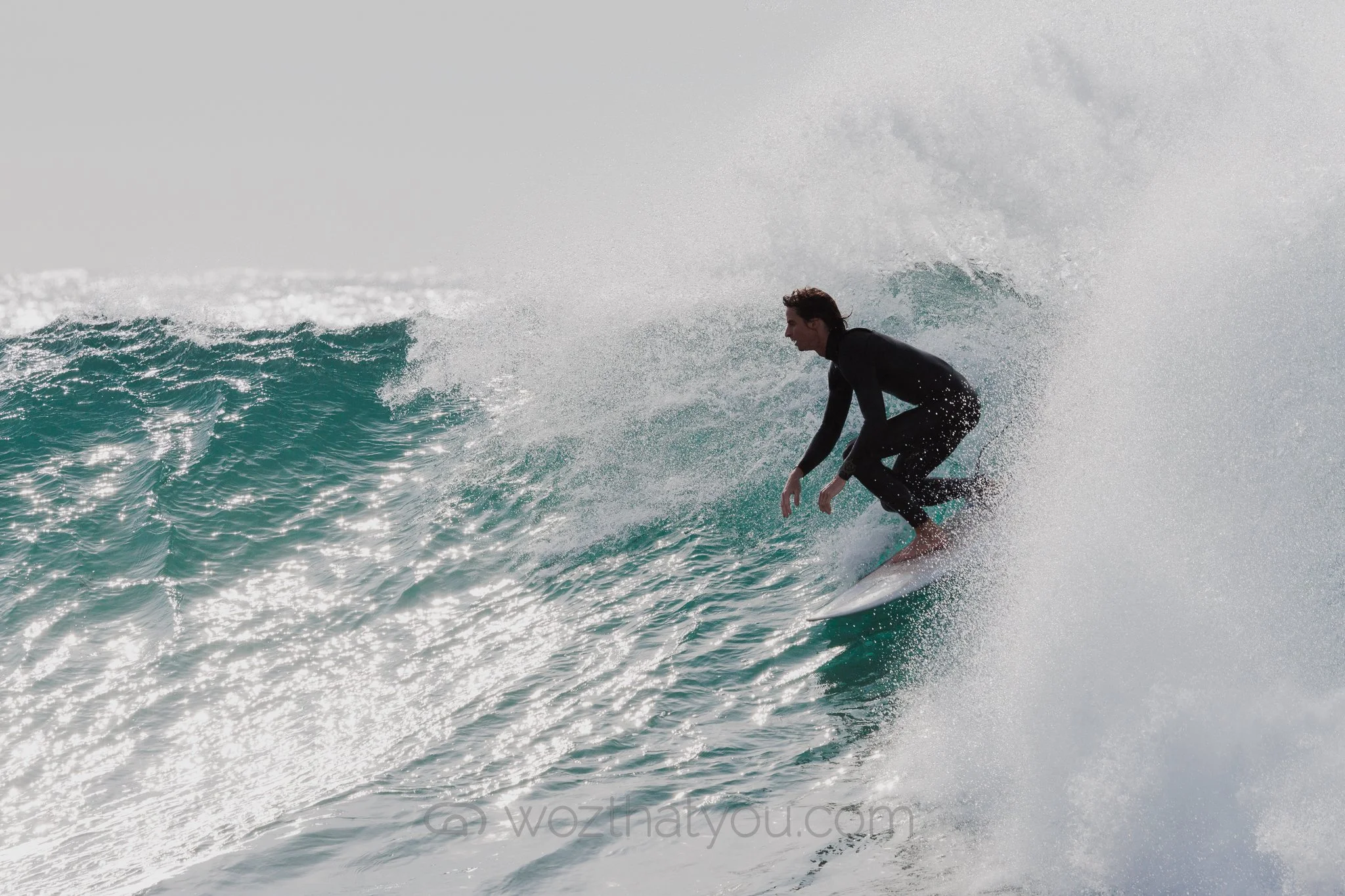 A man in a black wetsuit surfing on a wave.
