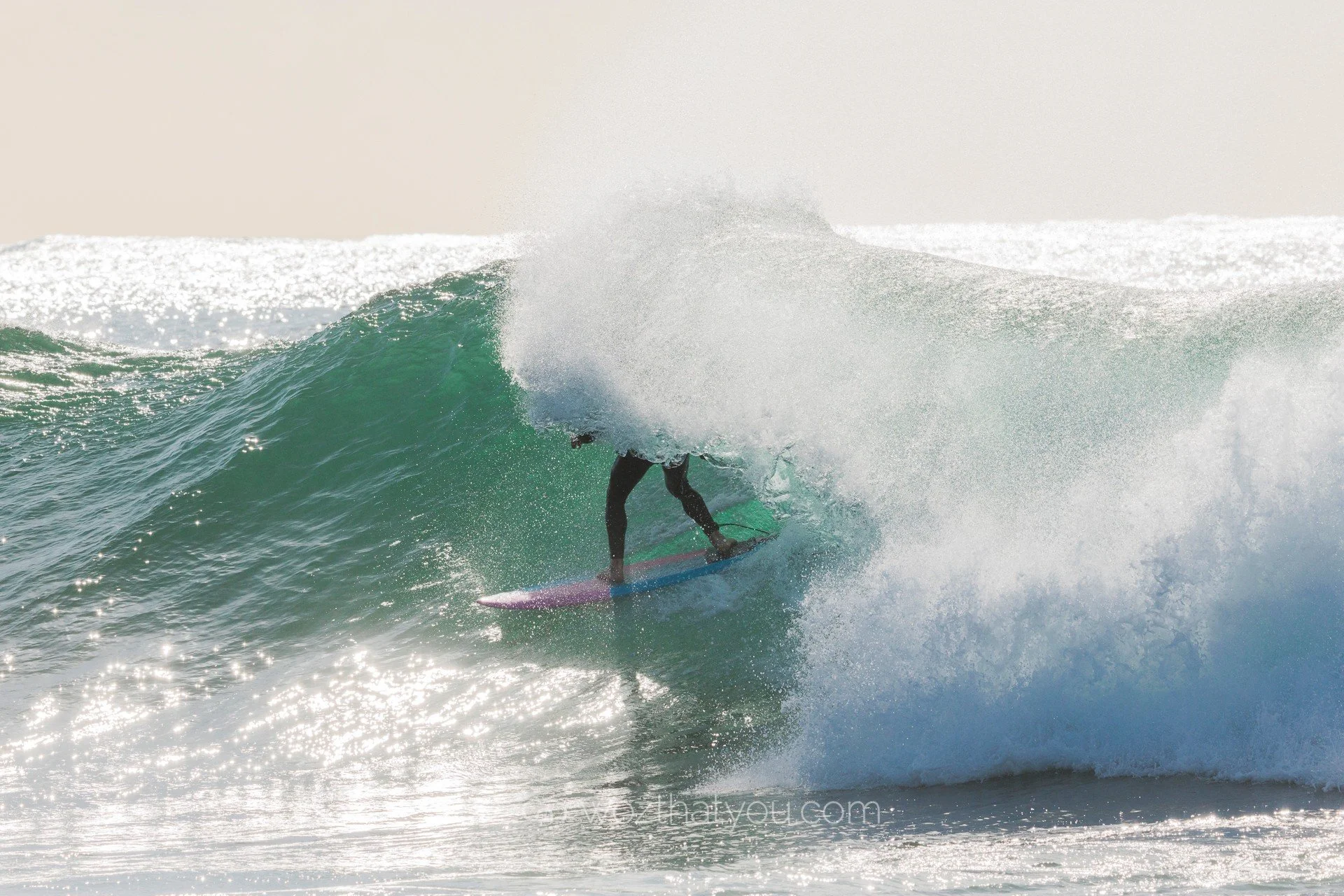 A person surfing on a wave in the ocean, with the waves crashing and spray in the air.