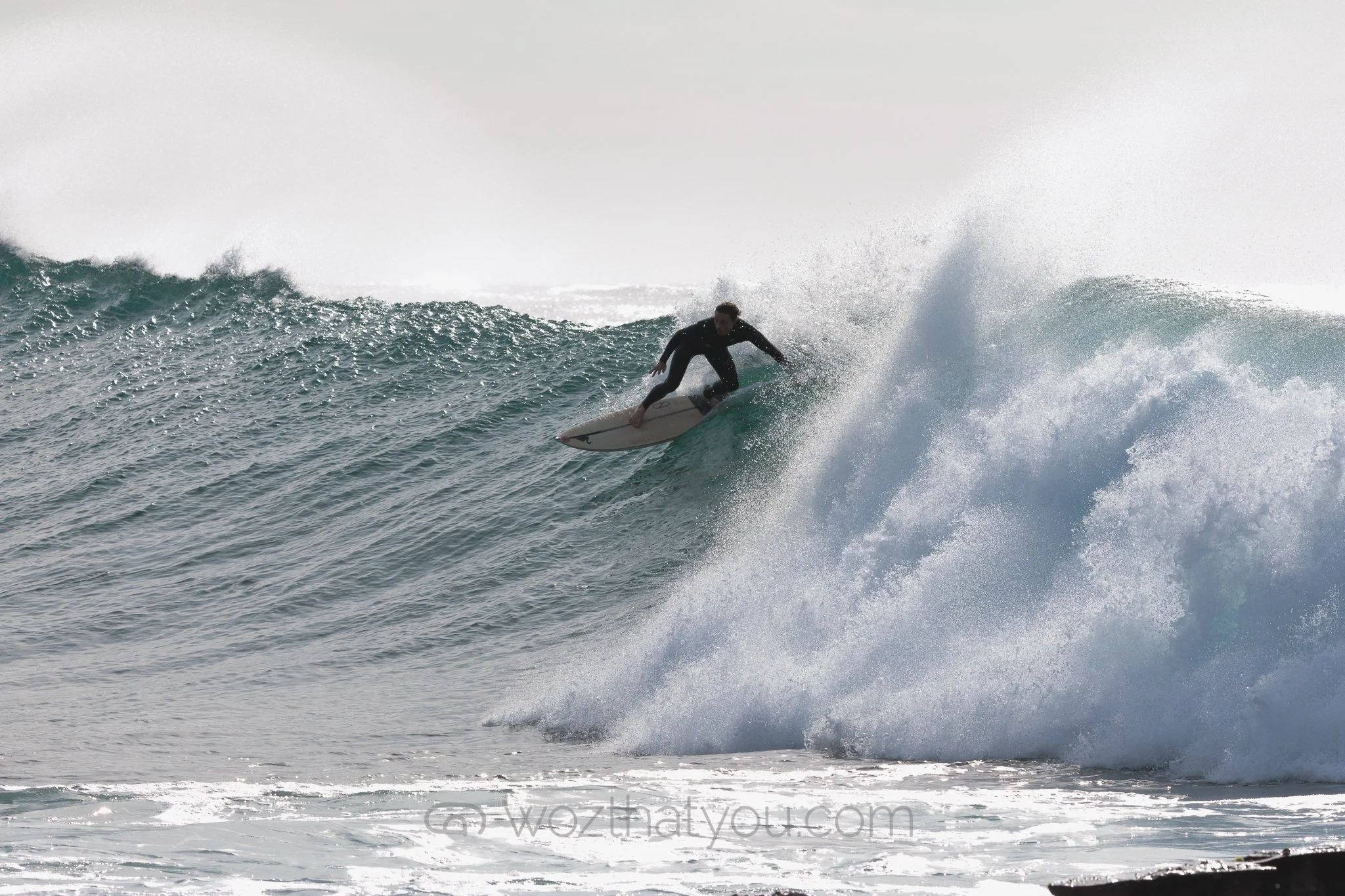 A person in a black wetsuit surfing on a wave in the ocean.