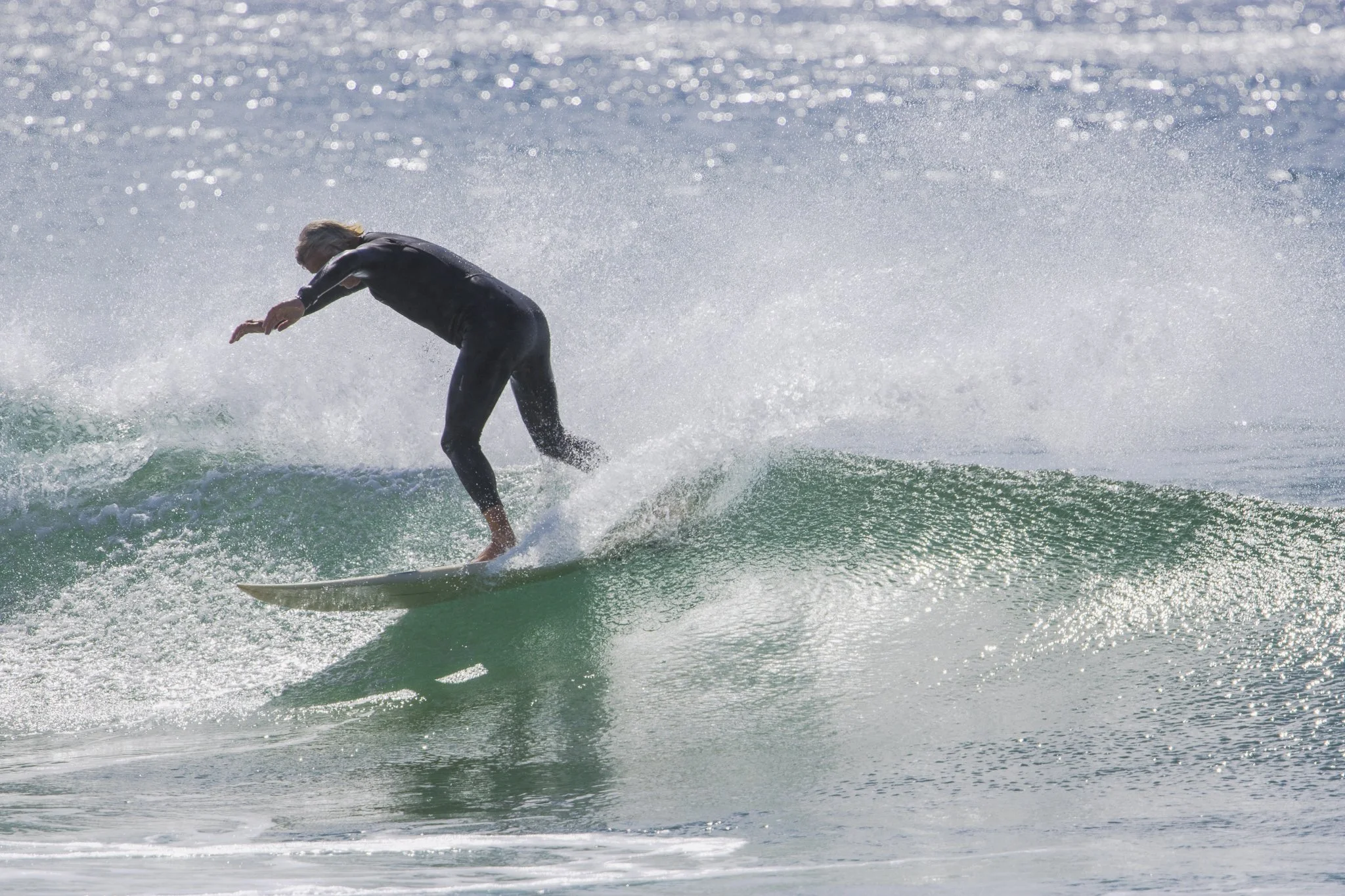 A person in a black wetsuit surfing on a small wave in the ocean during daylight.