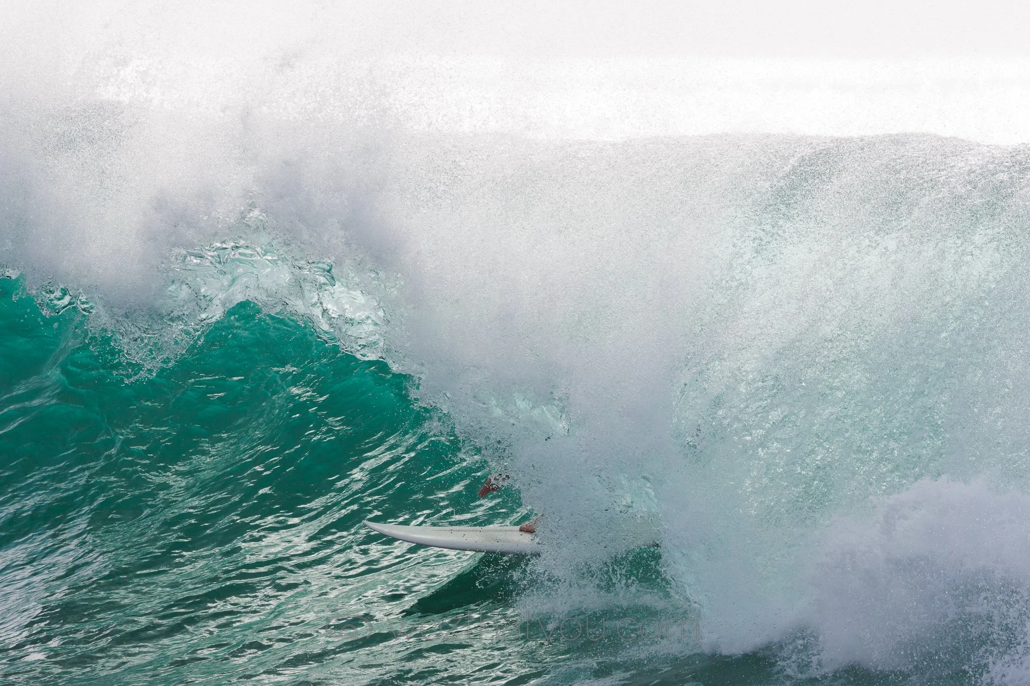A surfer falling off a surfboard inside a large breaking wave in the ocean.