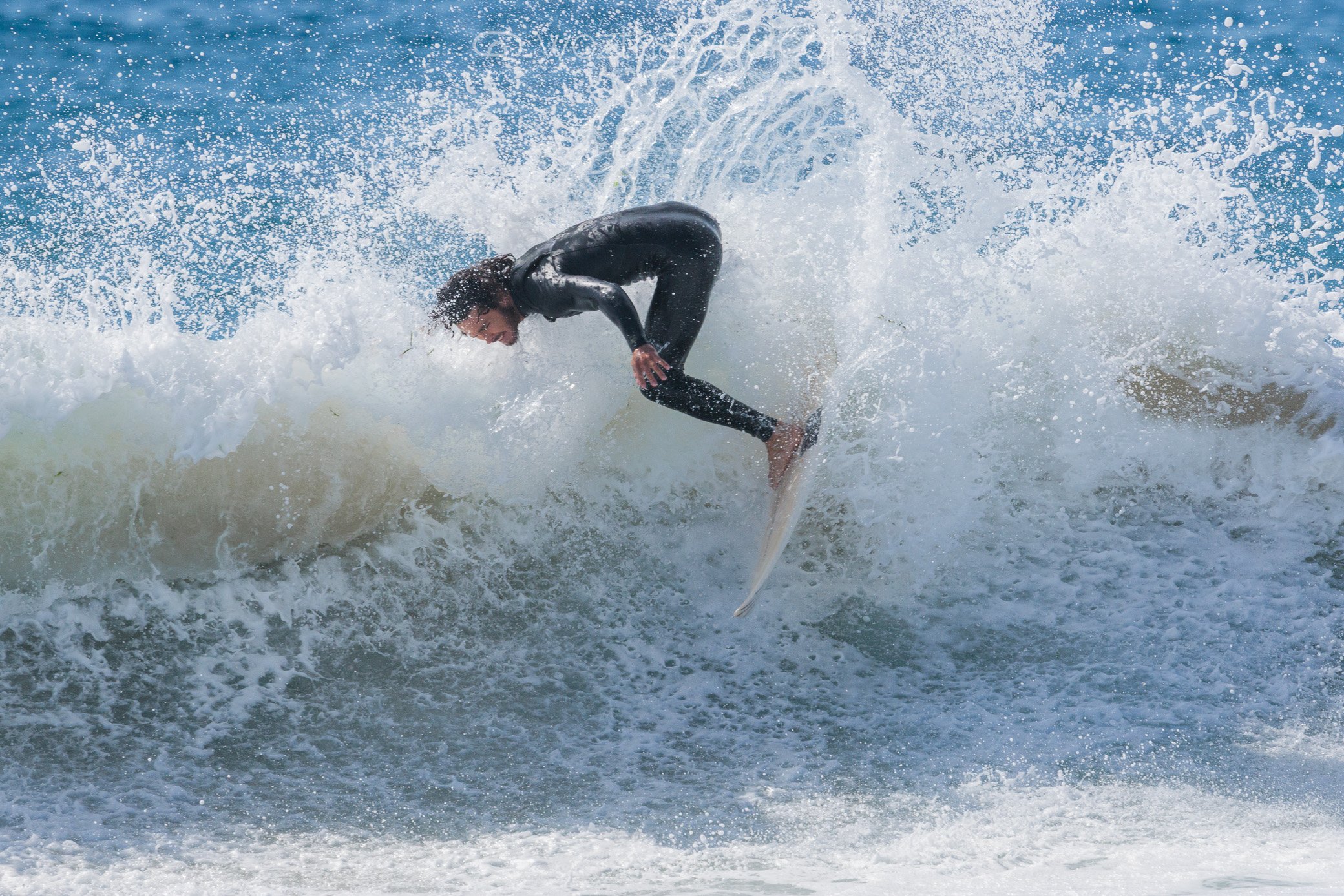 A person in a black wetsuit surfing on a wave in the ocean.