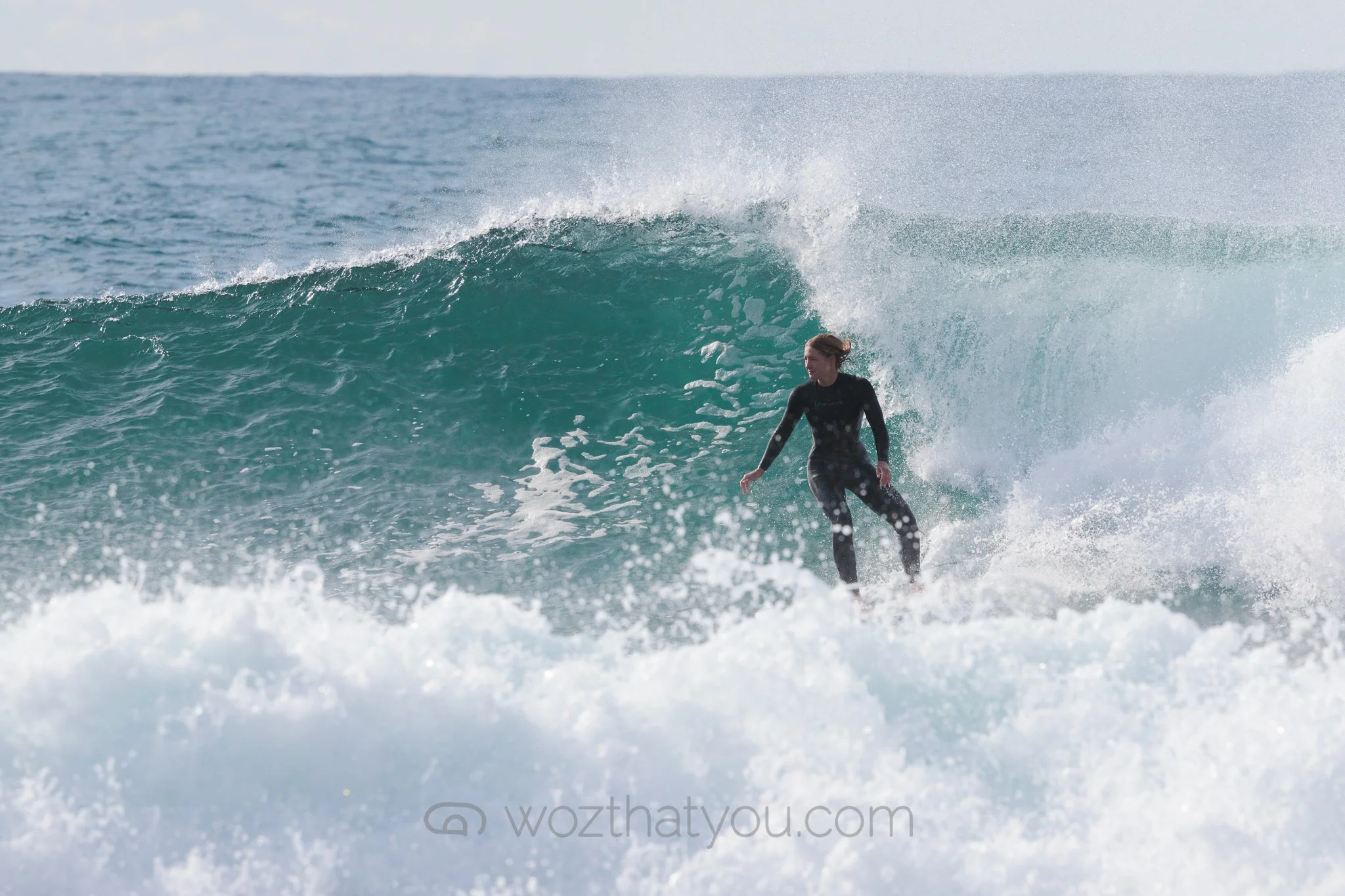 A woman surfing on a wave in the ocean, wearing a black wetsuit.