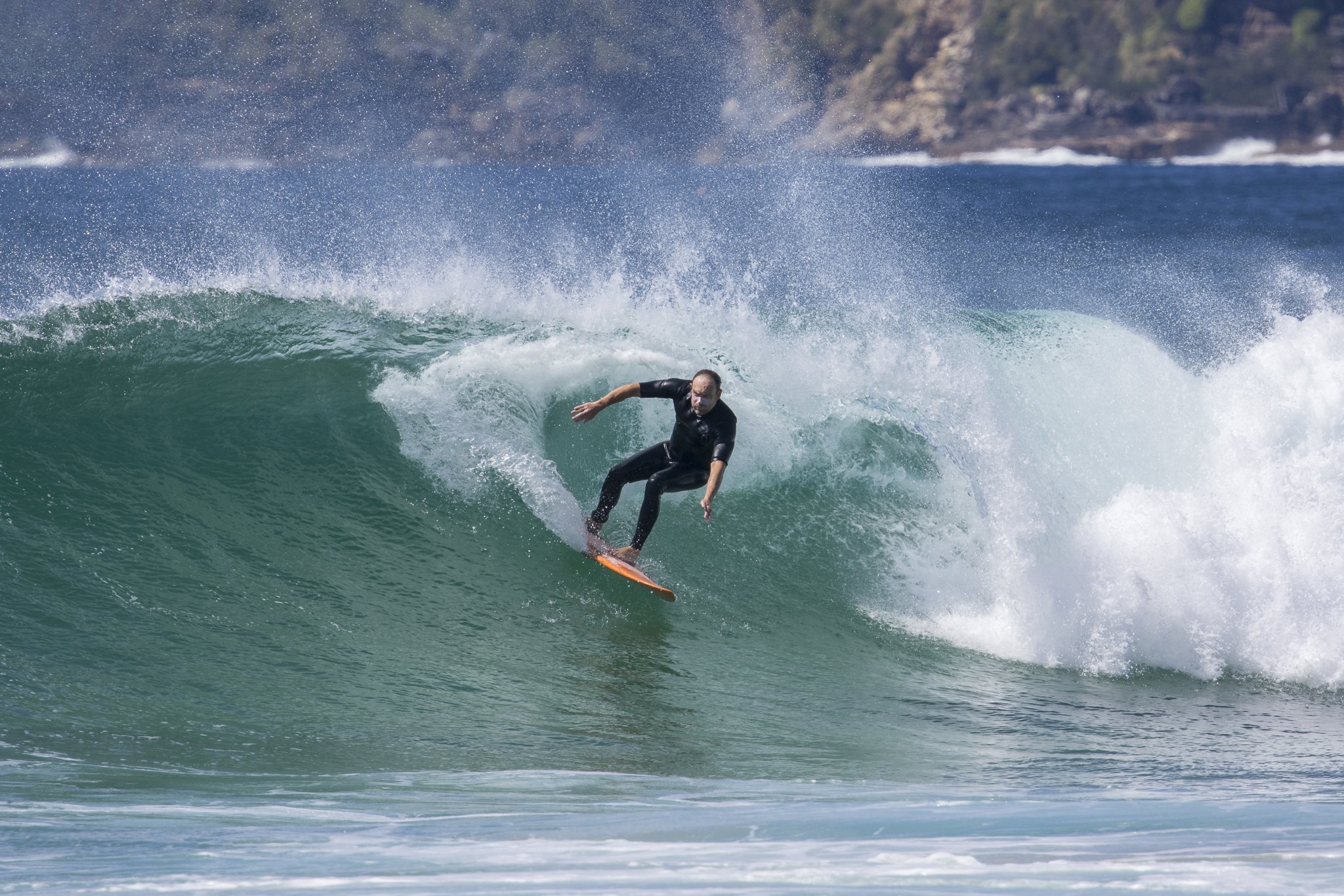 A person surfing on a wave in the ocean with a rocky coastline in the background.