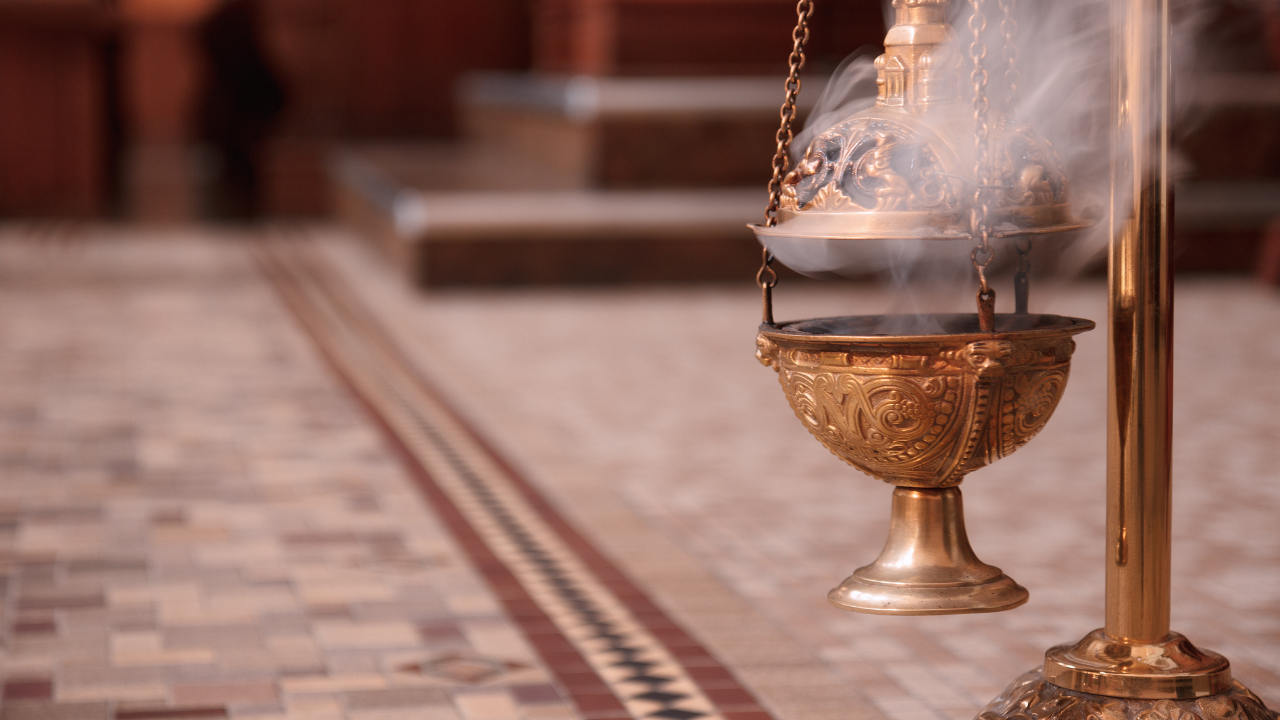 A gold incense holder with smoke rising, placed on a polished surface with a tiled floor in the background.