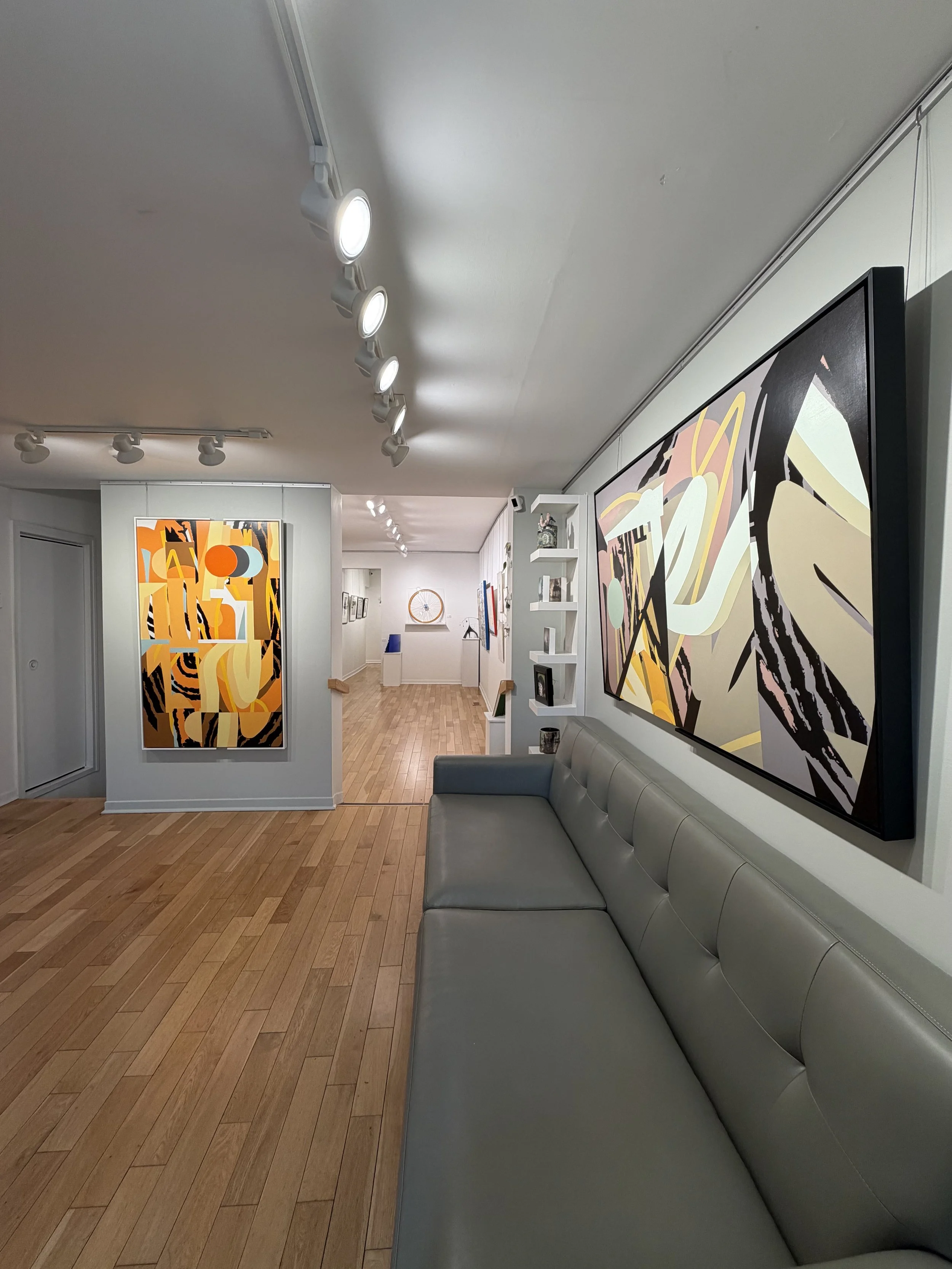 Modern living room with a white leather couch, a potted tree, abstract artwork on the wall, and a staircase on the left.