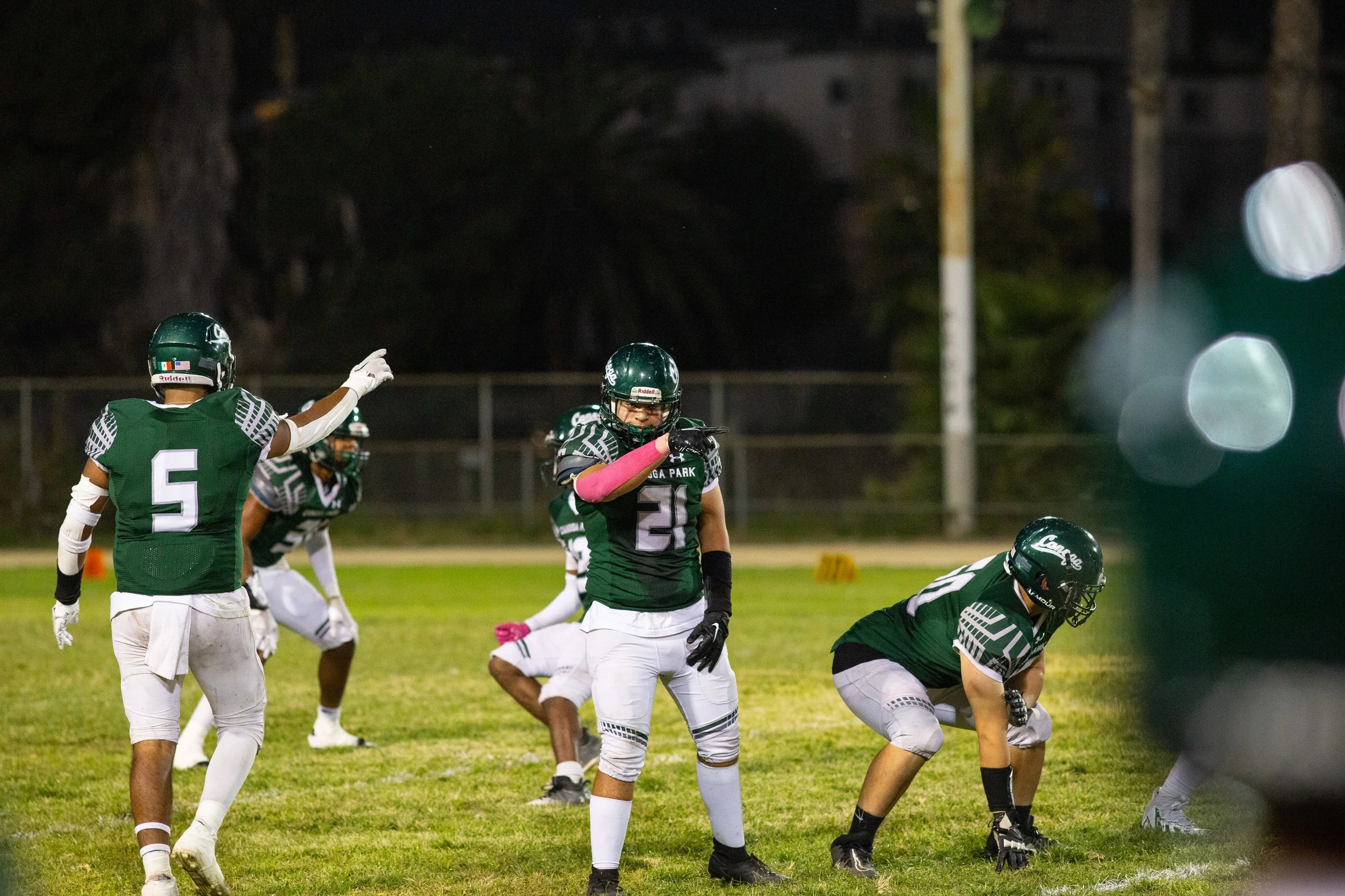 School photography. American football players on the field during a game at night, wearing green jerseys with white pants, and engaging in play.