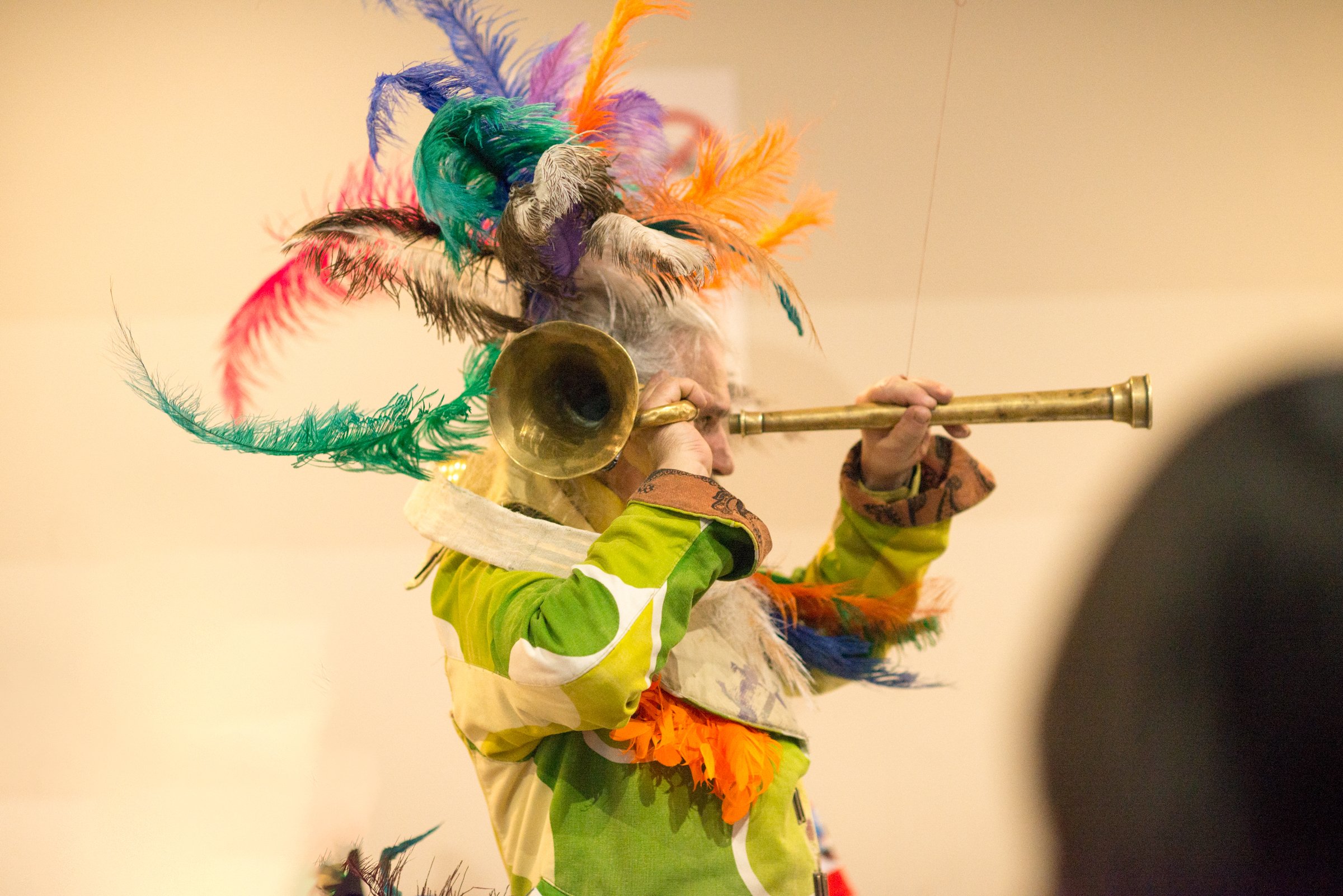 A person wearing a colorful feathered headdress and a yellow outfit playing a trumpet.