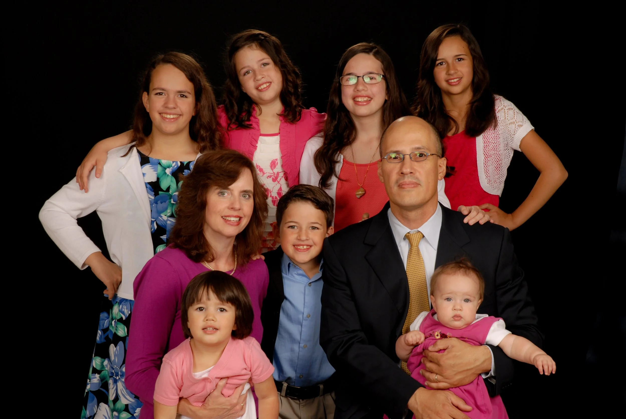 Family portrait with three adults and six children against a black background.