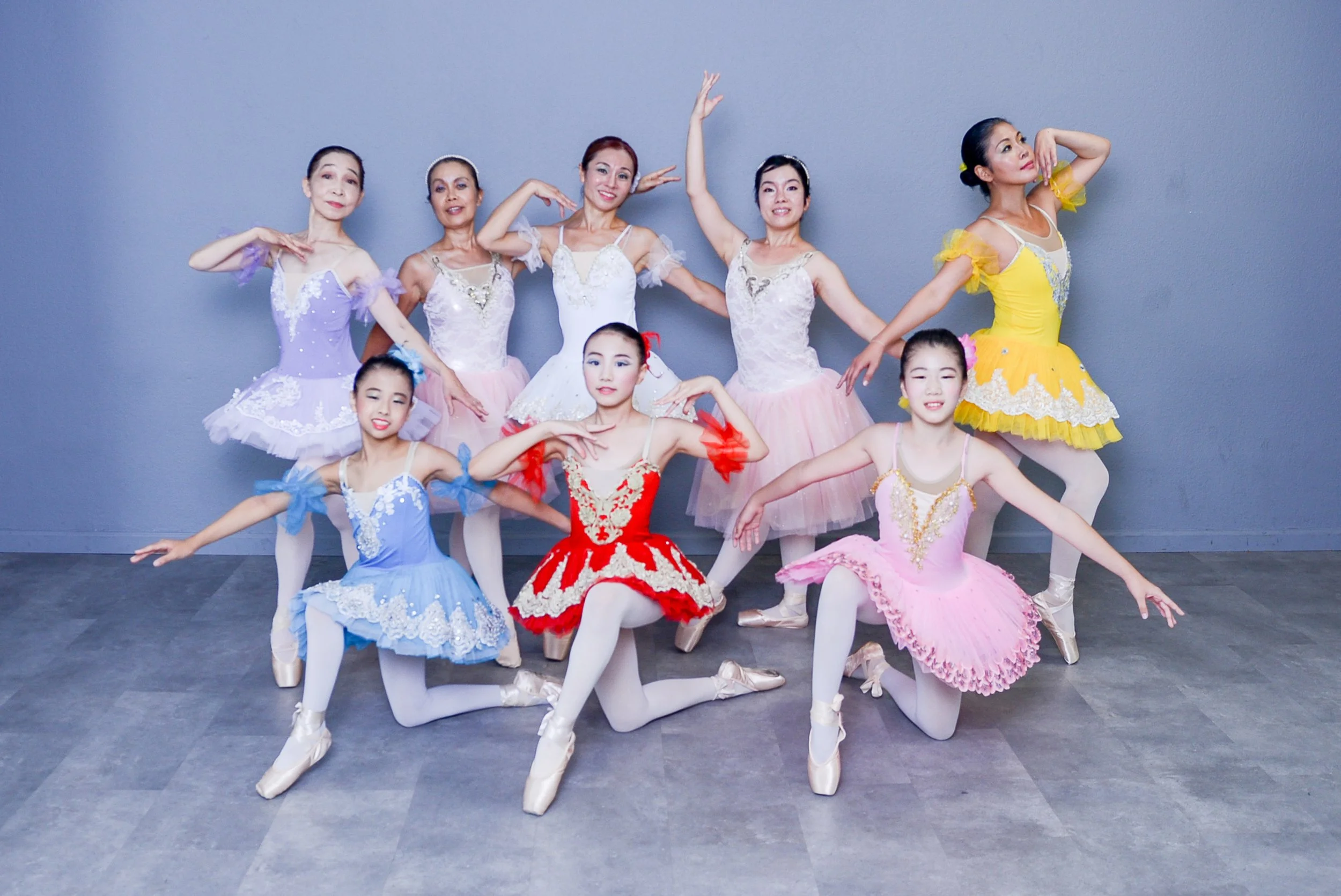 School photography. Group of young ballerinas in colorful tutus posing against a plain wall.