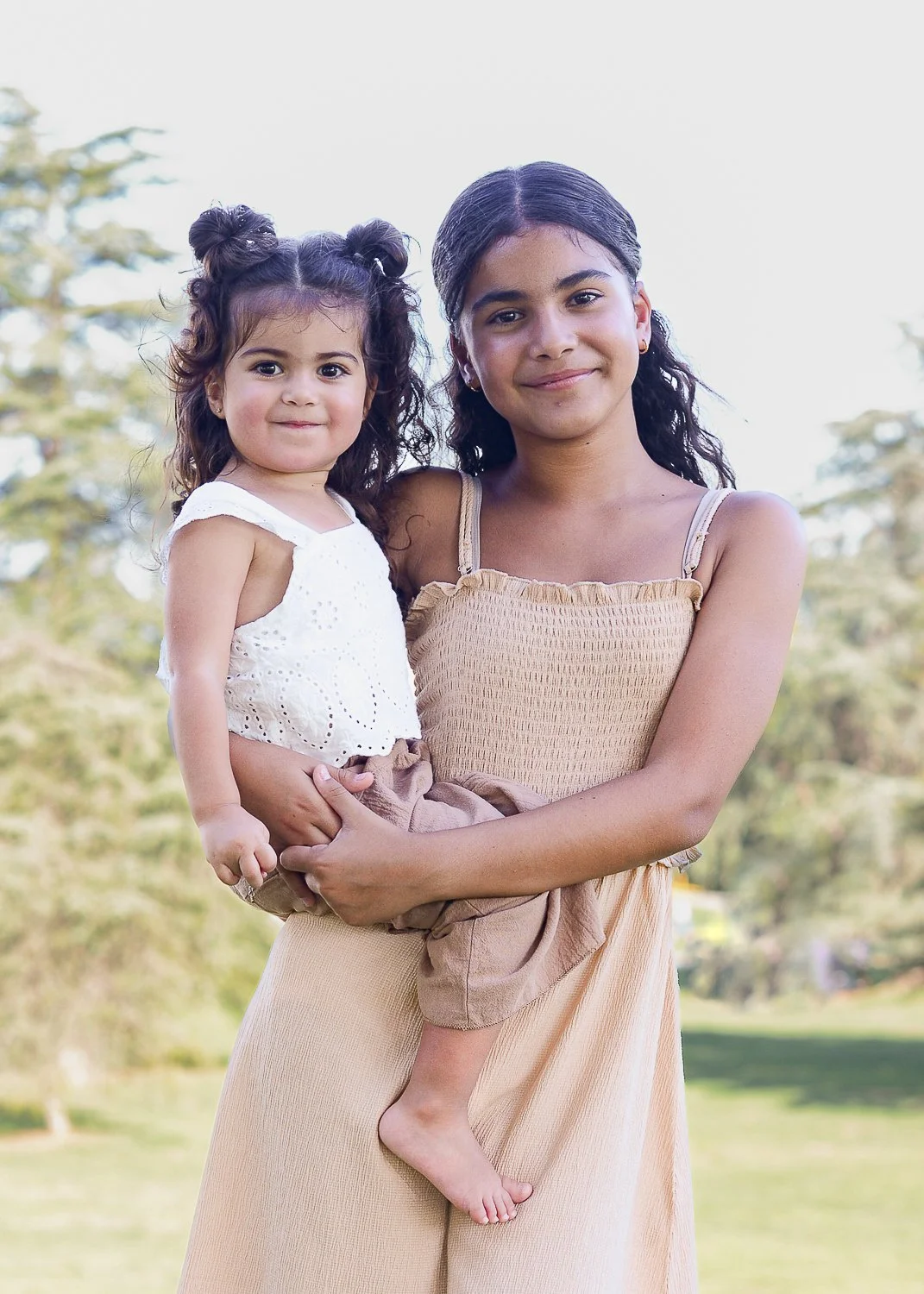 A young woman holding a small girl outside in a park during daytime.