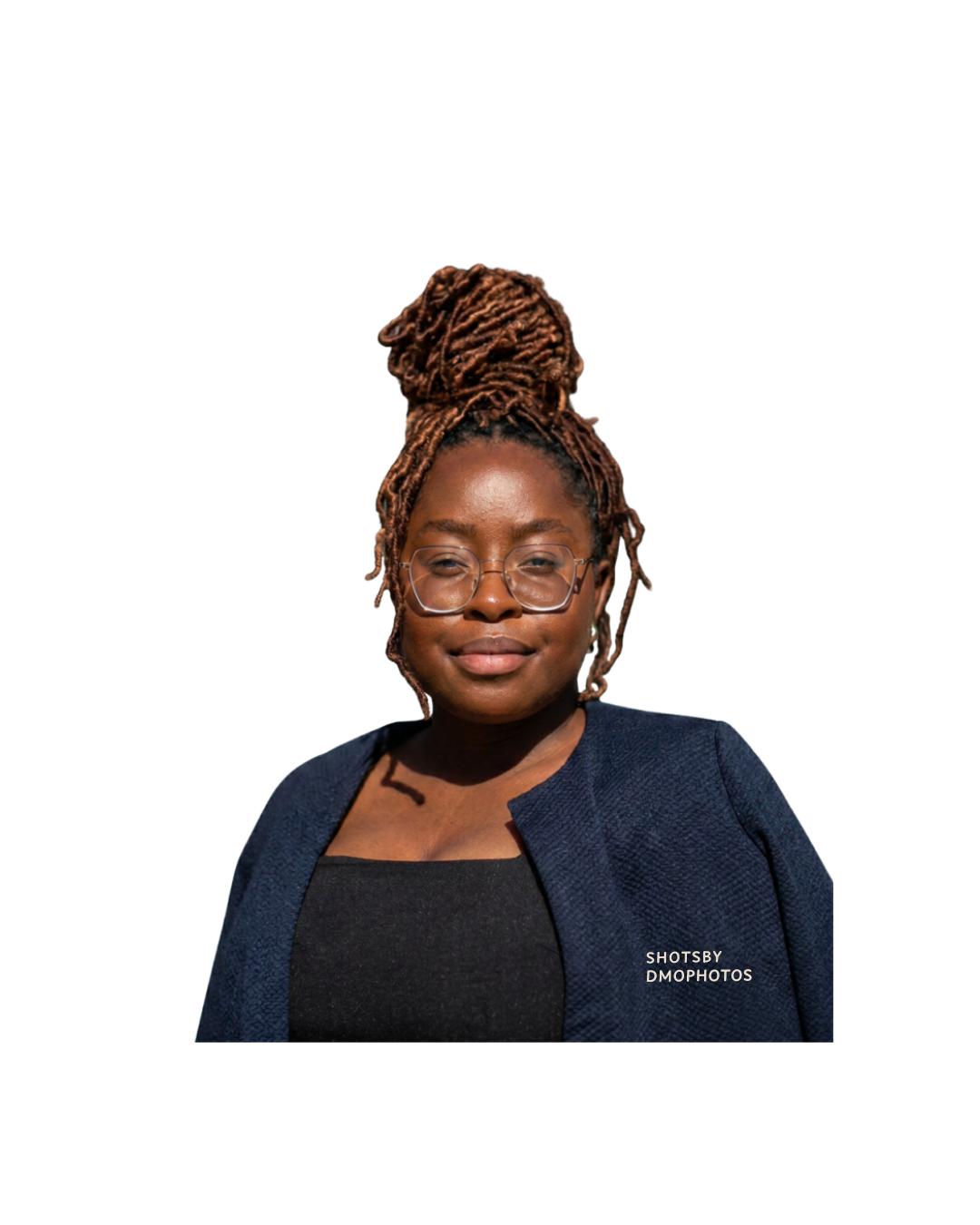 Portrait of a woman with glasses and dreadlocks styled up, wearing a navy blazer and black top, smiling slightly against a white background.