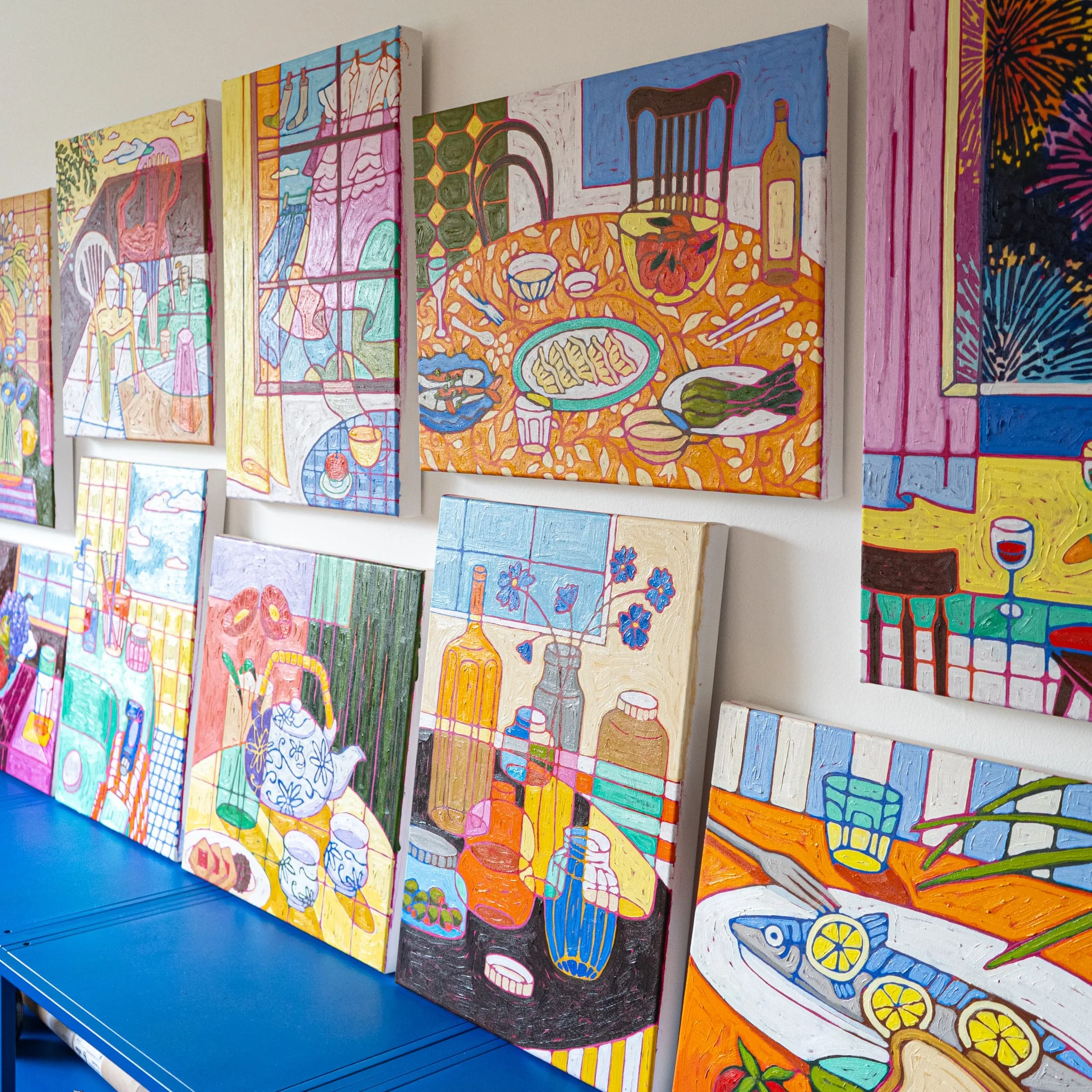Collection of colorful still life and interior paintings on a gallery wall, featuring tables of food, bottles, and objects.