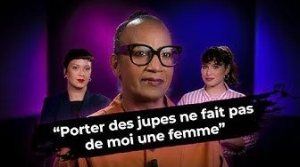 Trois femmes en studio avec un fond violet et bleu, deux d'entre elles en arrière-plan, tenant une bannière qui dit : « Porter des jupes ne fait pas de moi une femme ».