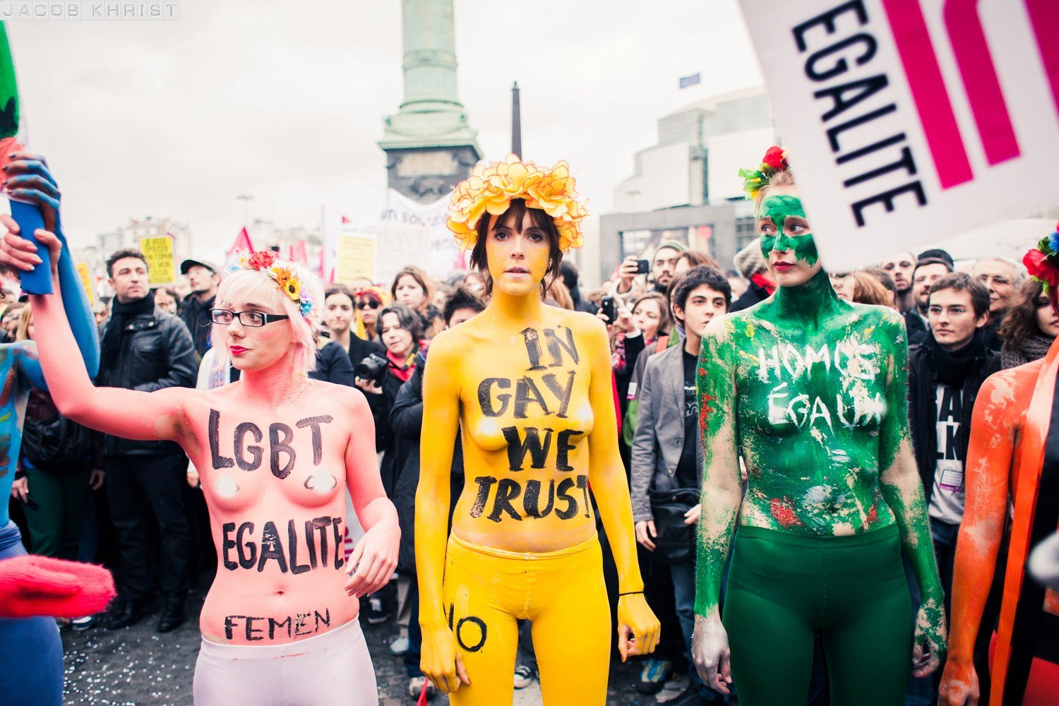 Groupe de manifestants lors d'une marche pour les droits LGBTQ+ avec des personnes peintes en corps et portant des messages comme «LGBT EQUALITY FEMIN» et «IN GAY WE TRUST» dans un lieu public. femen Marguerite Stern