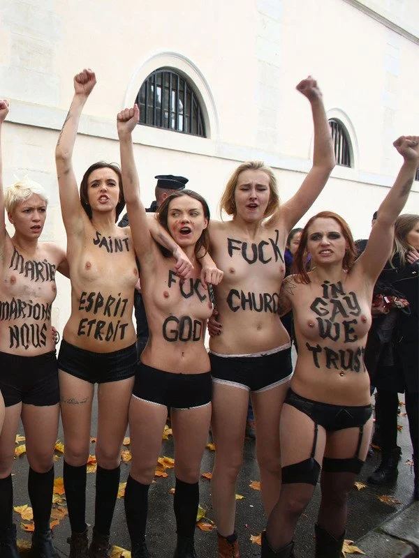 Femmes seins nus avec des messages écrits sur leur poitrine, levant le poing lors d'une manifestation.