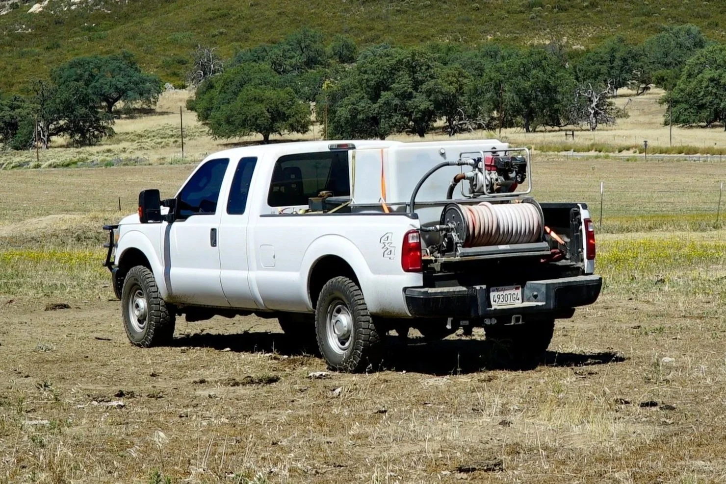 white 4x4 truck with fire suppression skid unit in the back. Water tank in truck with hose reel.