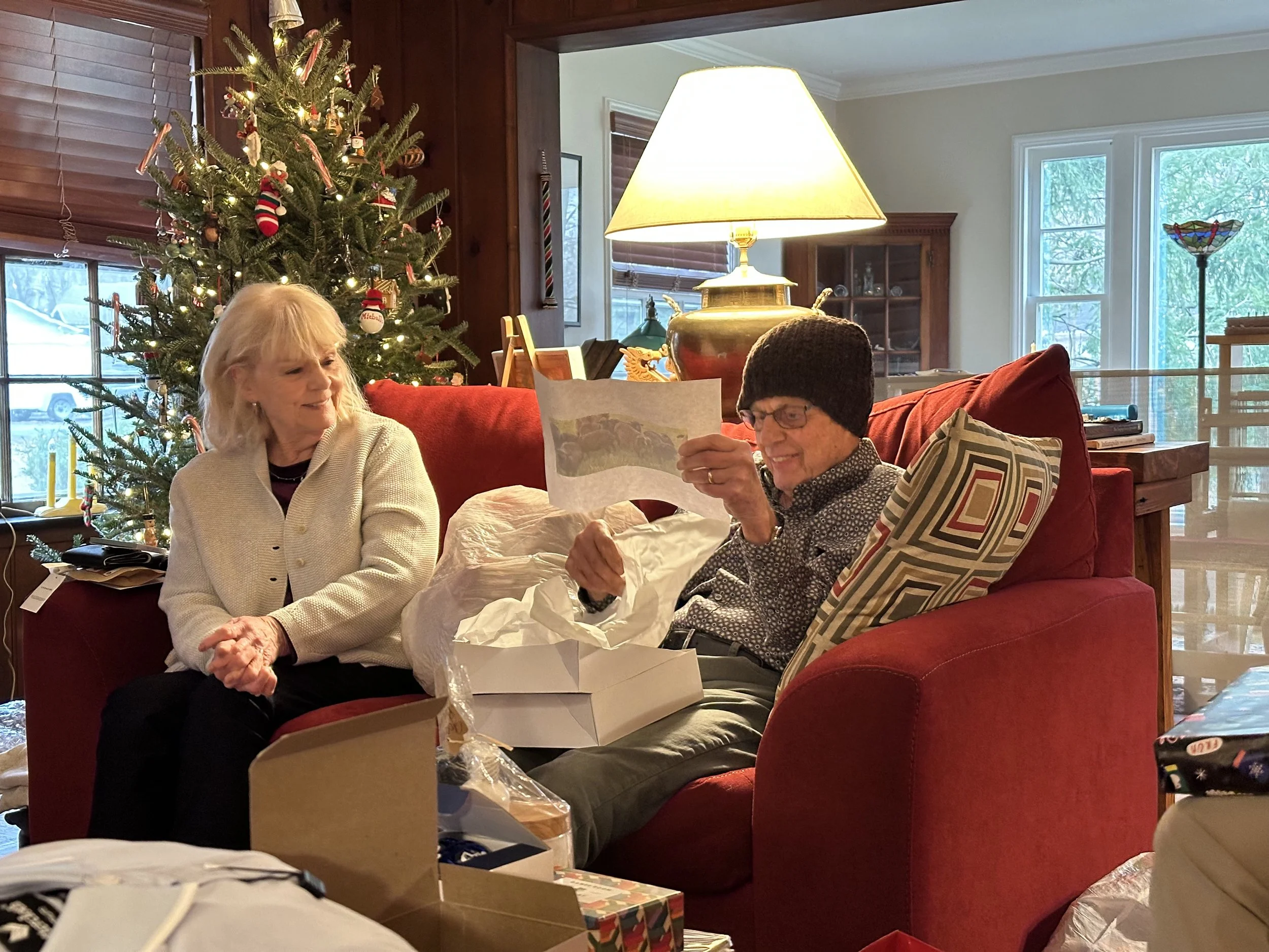 Michelle's parents with her dad wearing the knit beaning and holind the photo of the sheep