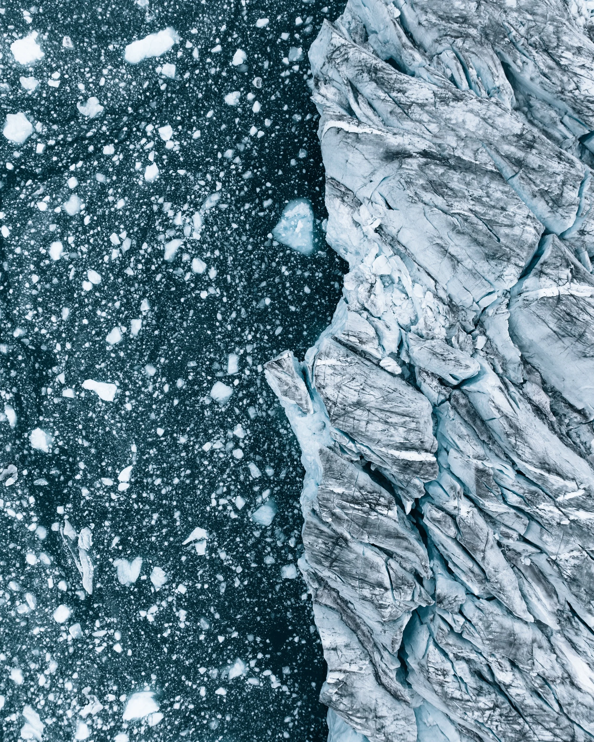 An aerial view of a glacier and icy water with floating ice chunks and crevices in the ice.