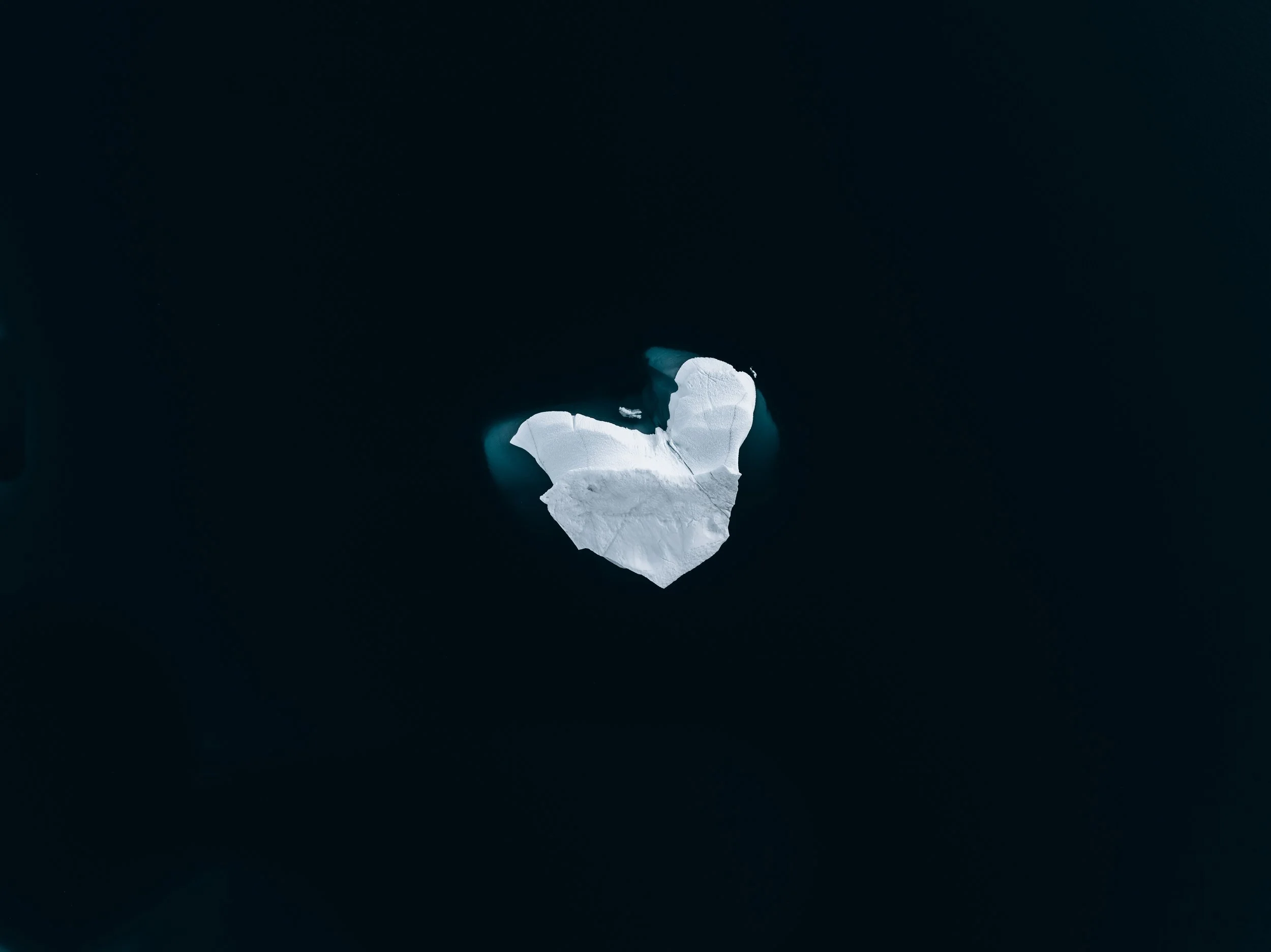 An iceberg in the shape of a heart floating in dark ocean water.