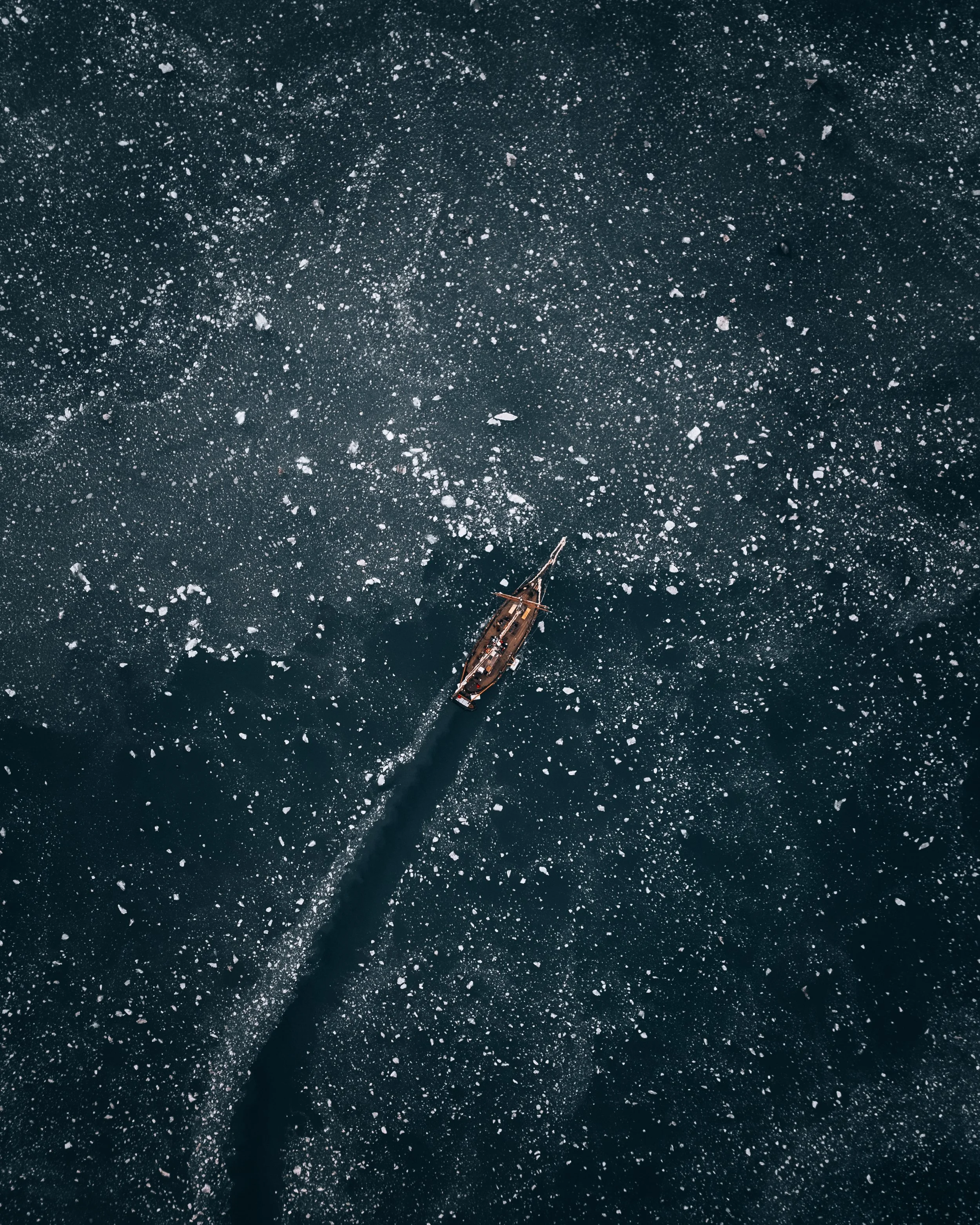 A boat sailing through icy water with ice chunks floating on the surface.