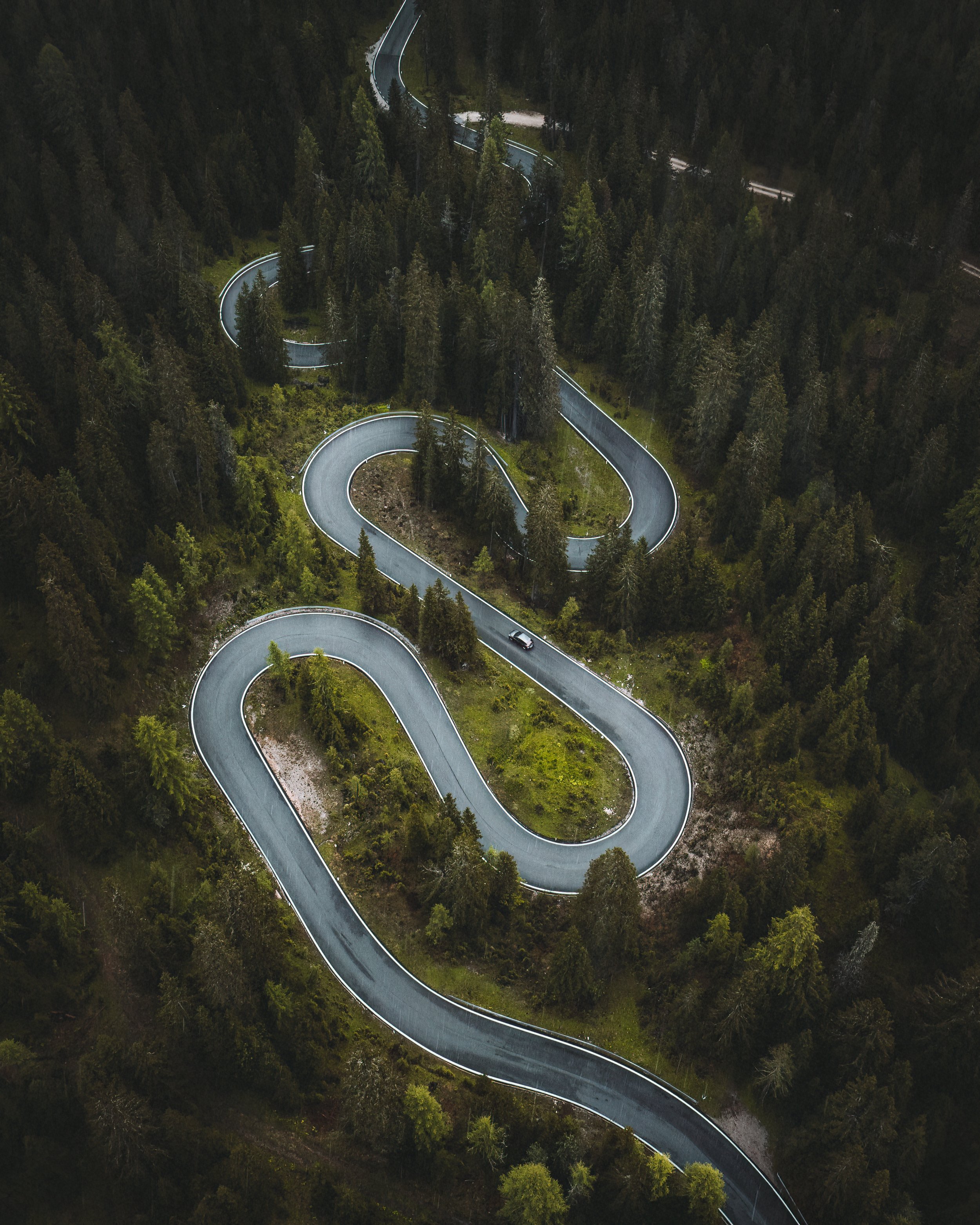 An aerial view of a winding mountain road through a forest with trees and greenery.
