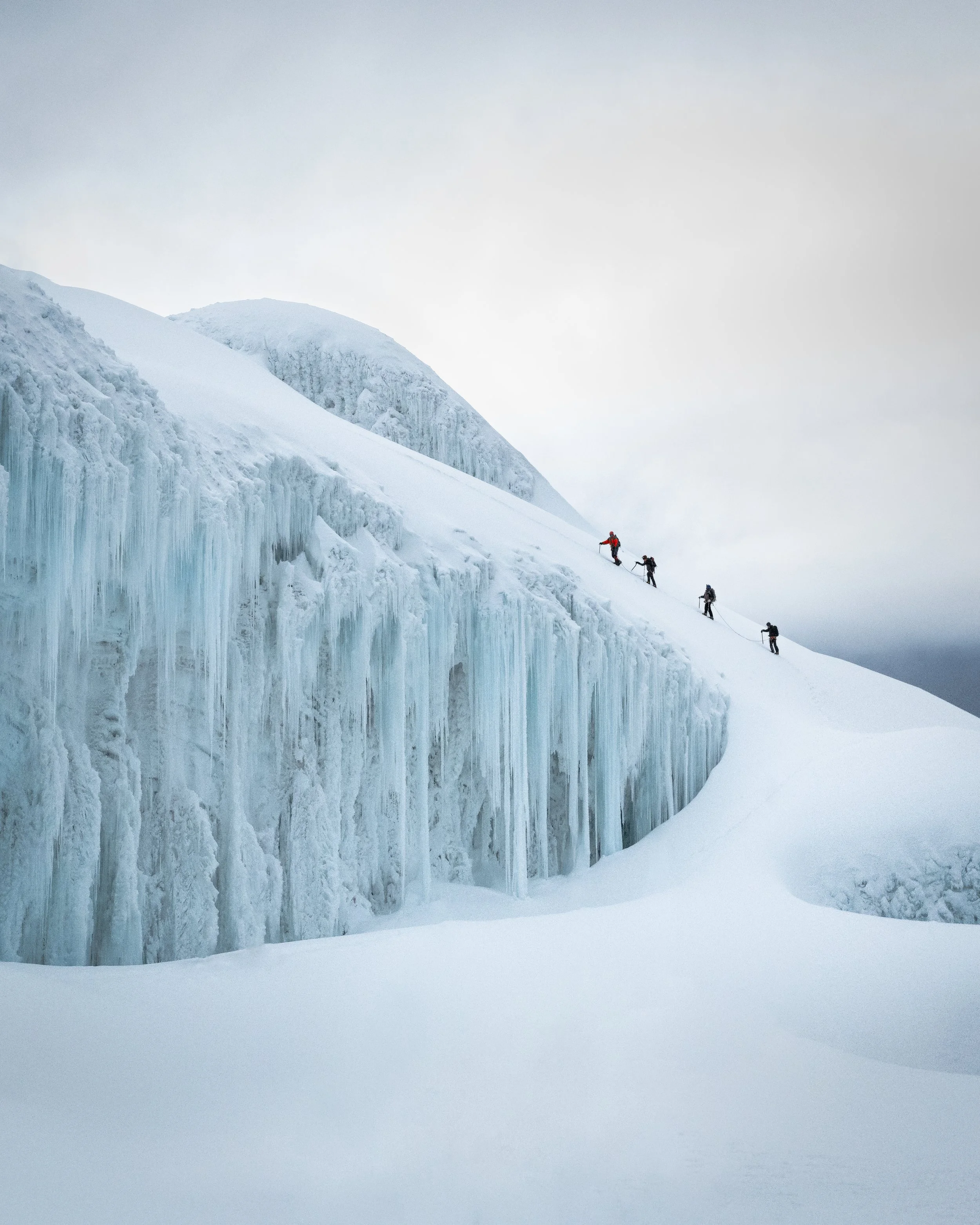 Group of climbers ascending a snow-covered, icy mountain slope with ice formations.