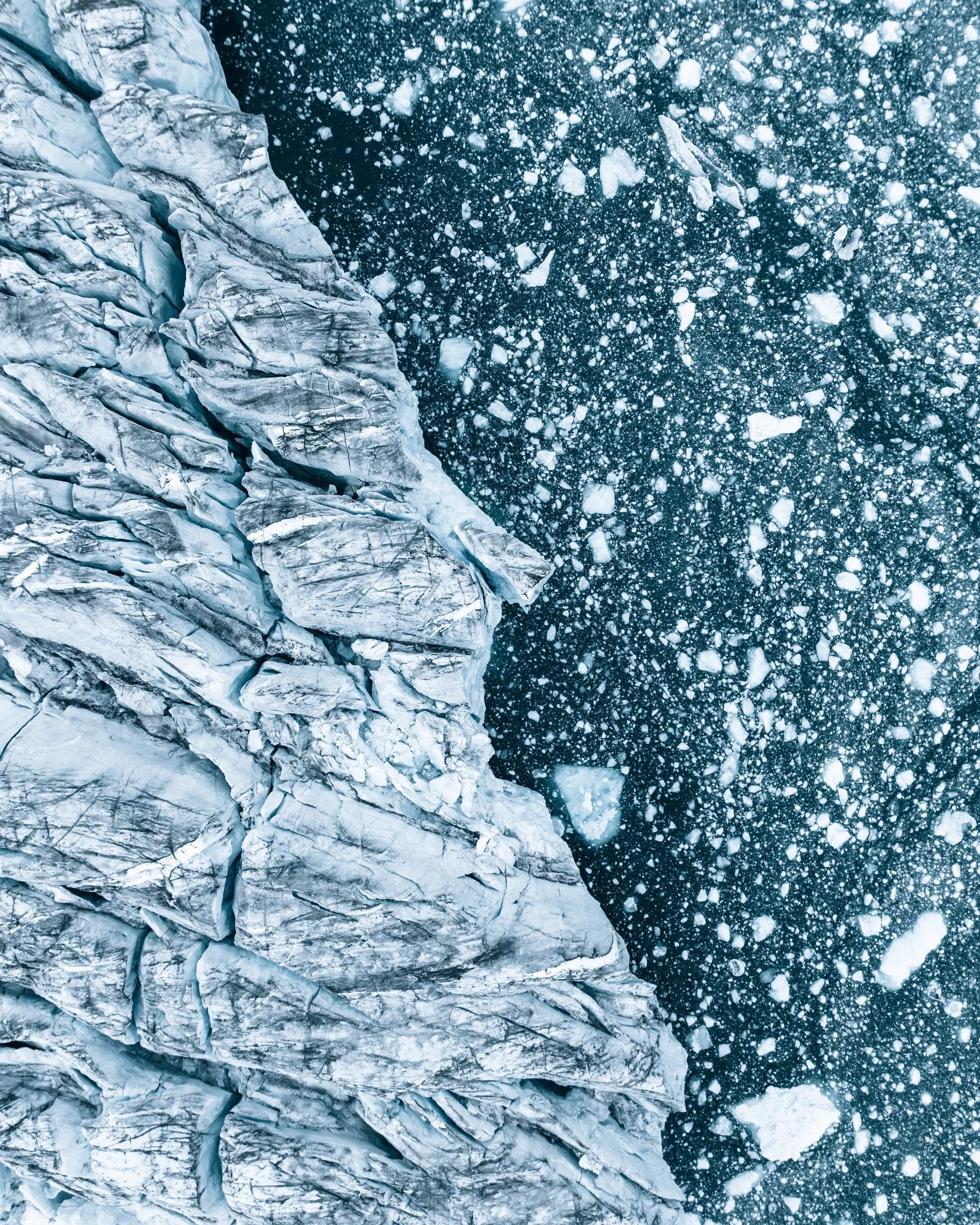 Aerial view of icy glacier meeting frozen, ice-covered water with floating ice chunks.