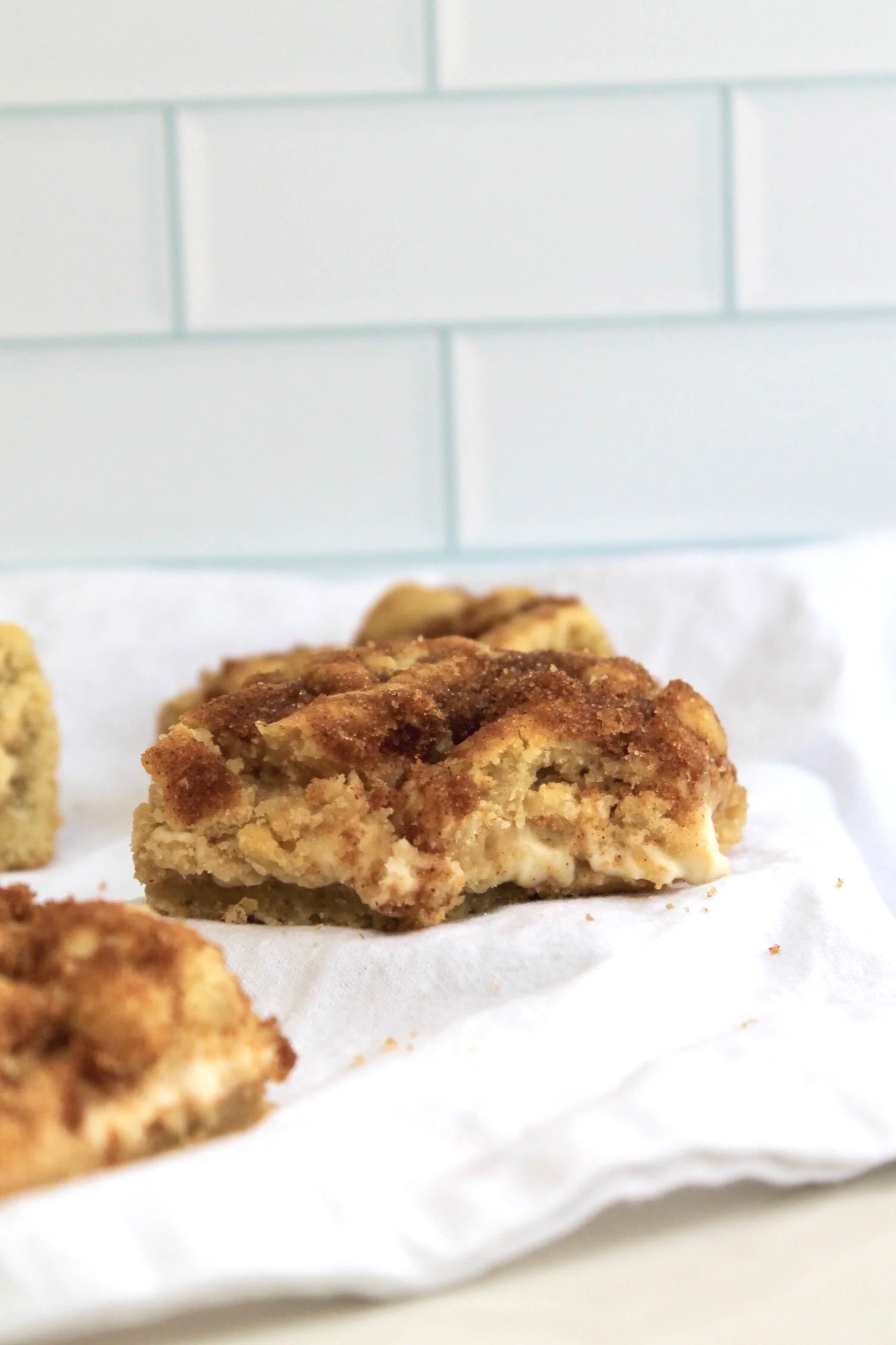 Close-up of crumbly cinnamon pastry on a white napkin with a tiled background.
