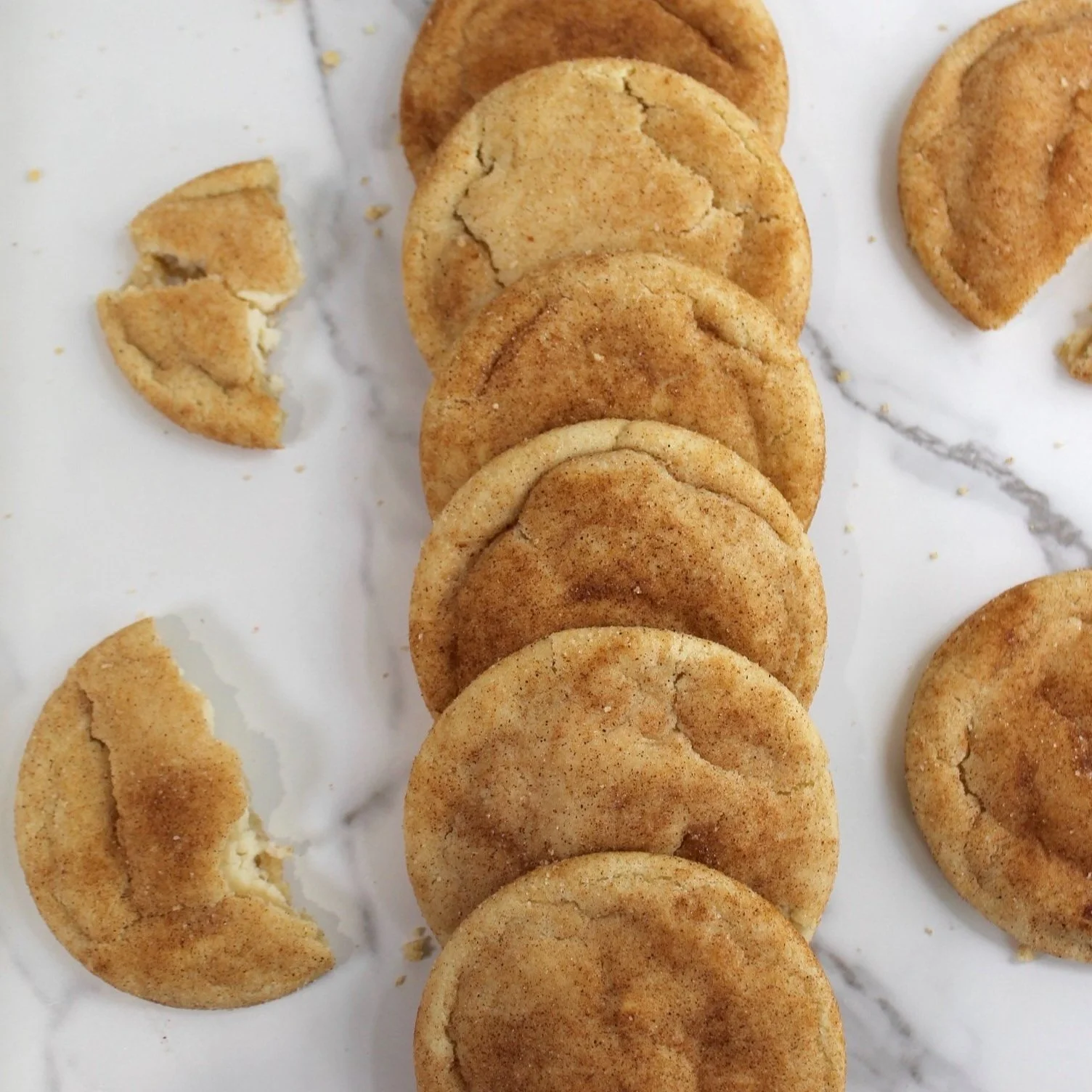 Snickerdoodle cookies arranged in a row on a marble surface, with one partially eaten cookie nearby.