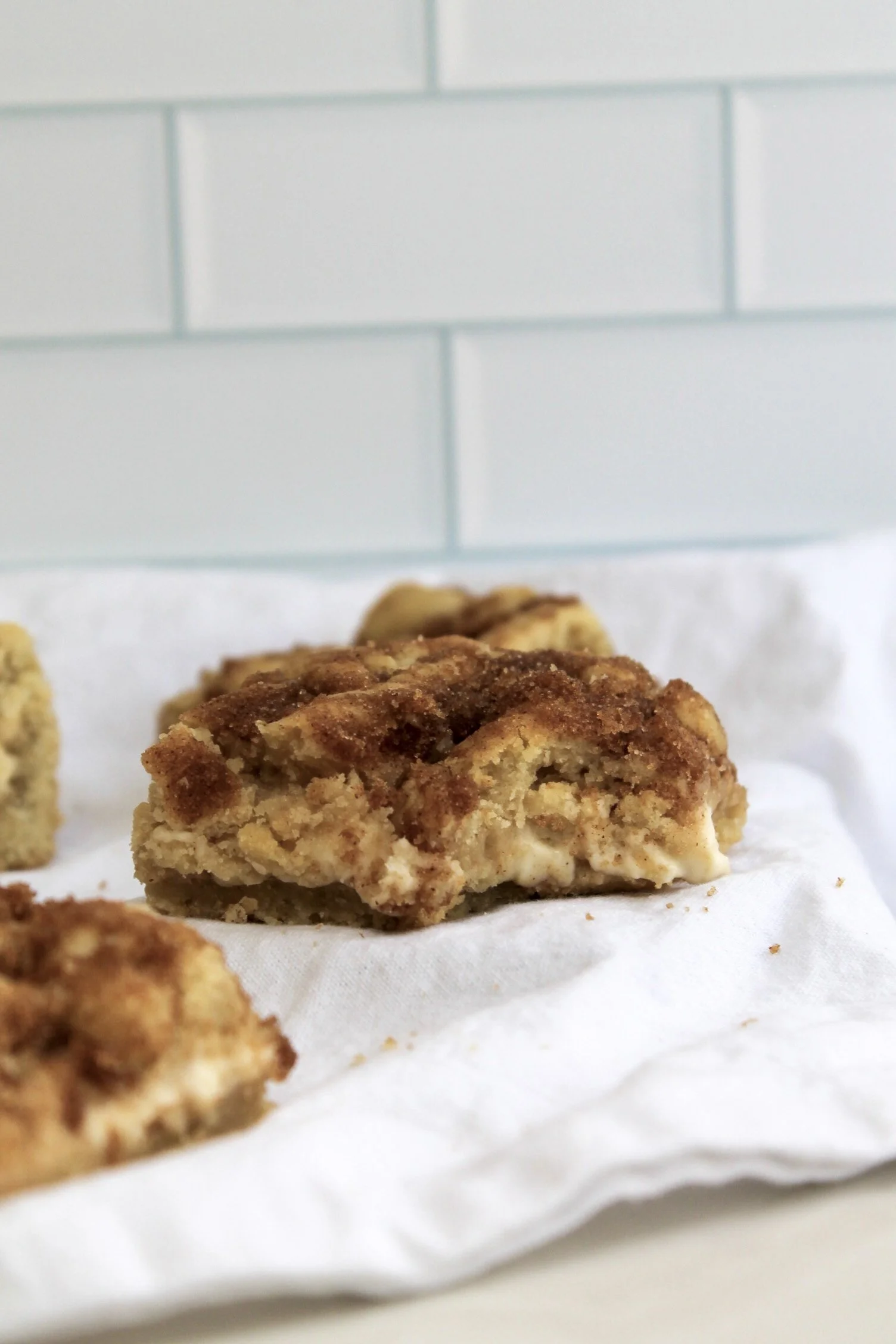Close-up of crumbly cinnamon pastry on a white napkin with a tiled background.