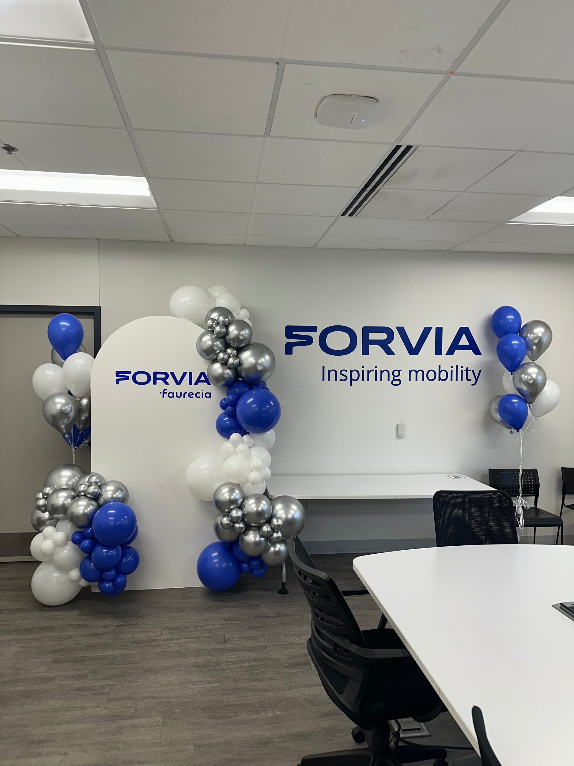 Office celebration decor featuring balloons in blue, white, and silver around a white wall with the FORVIA logo and the words "Inspiring mobility".