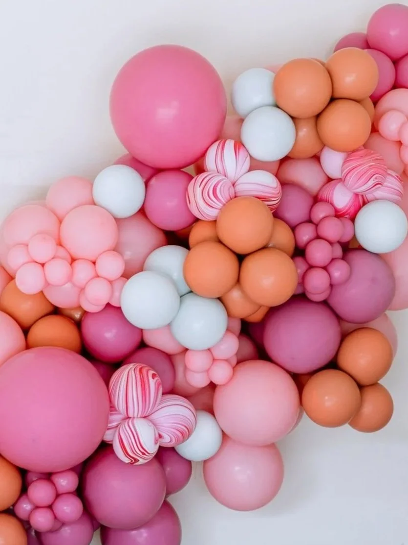 A variety of pink, orange, white, and striped balloons arranged together.