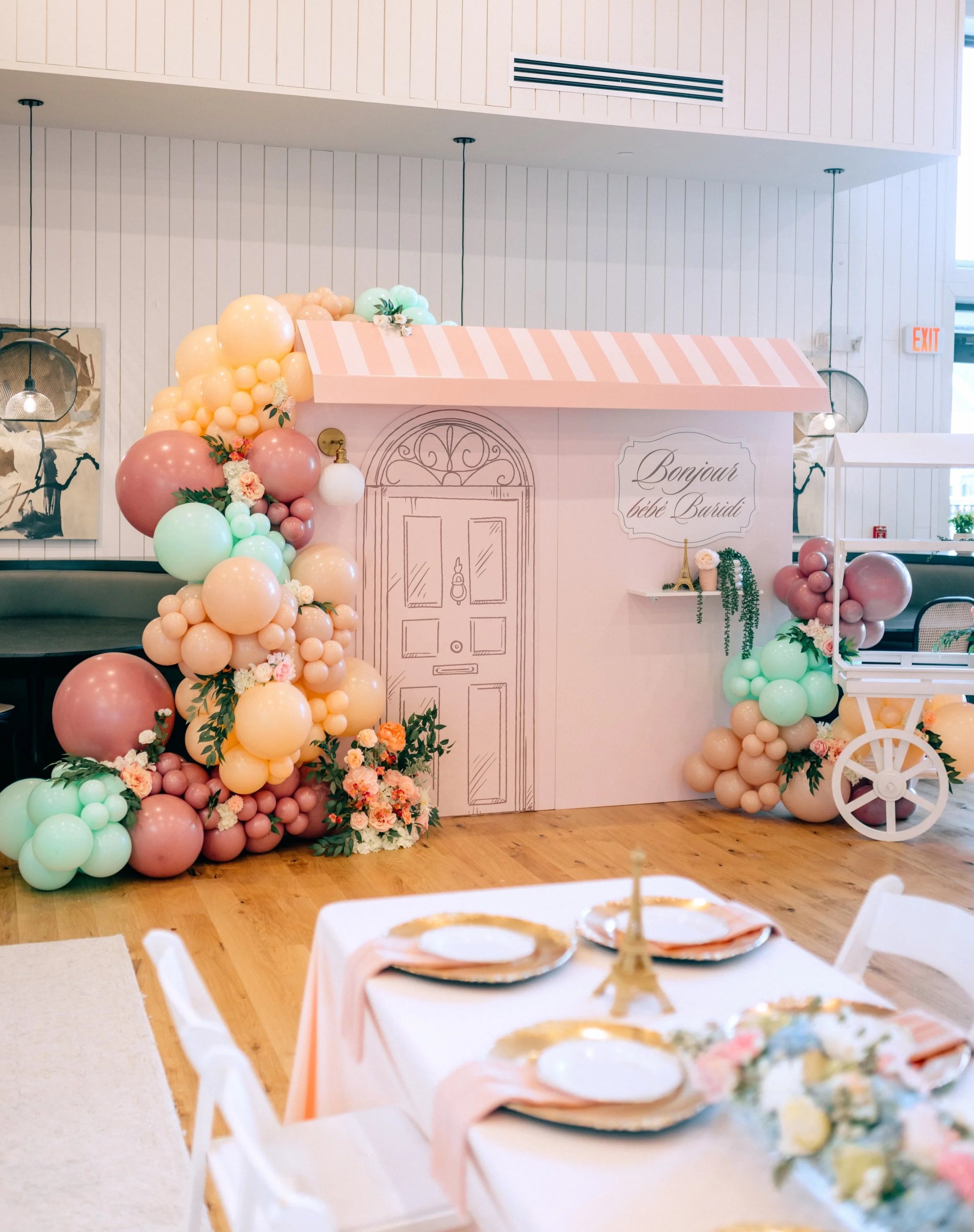 Decorated backdrop with pastel-colored balloons, flowers, and a hand-drawn door, for a baby shower celebration.
