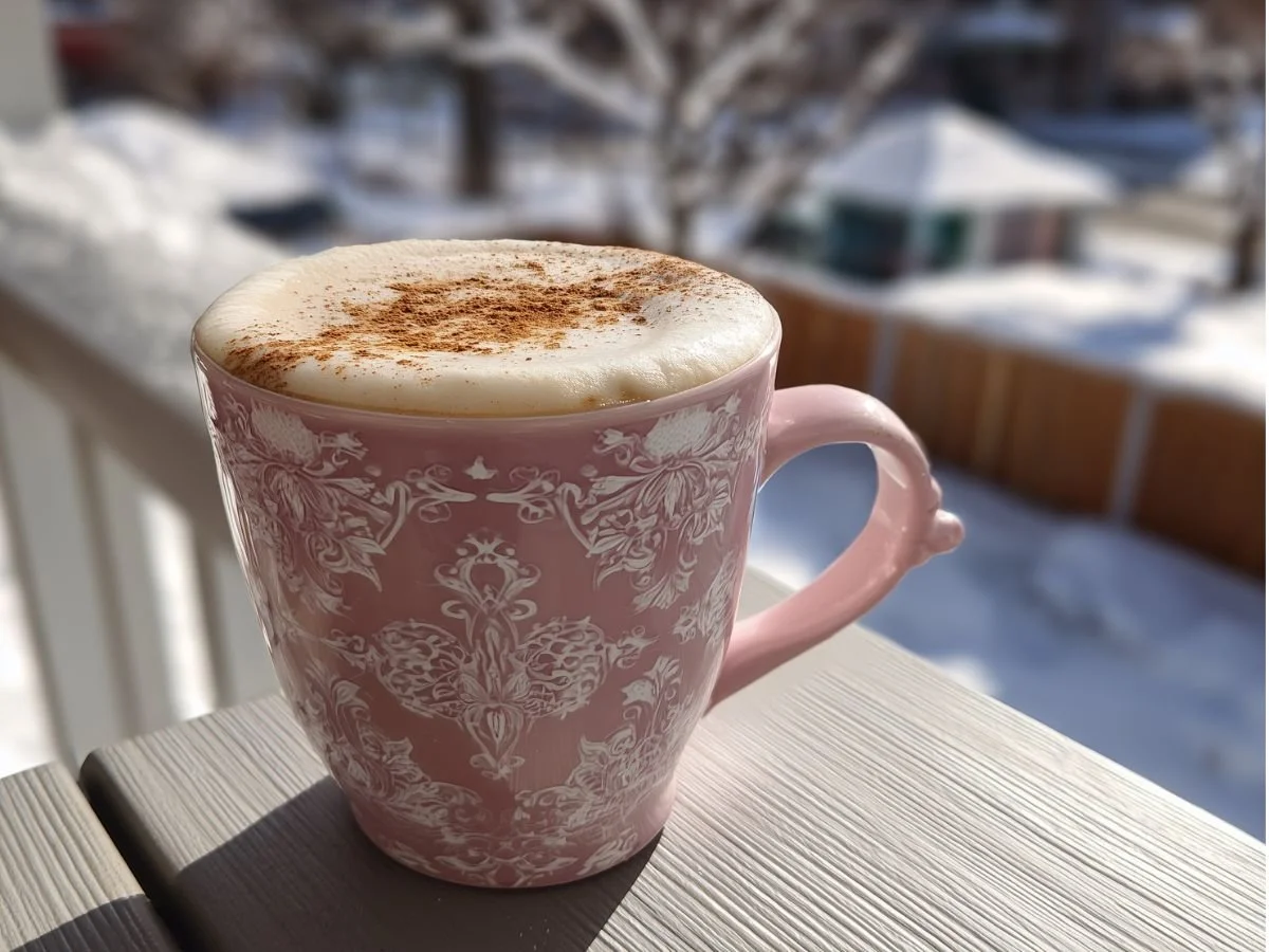 Cinnamon oat milk steamer in a porcelain mug on an outdoor patio table with a winter background.