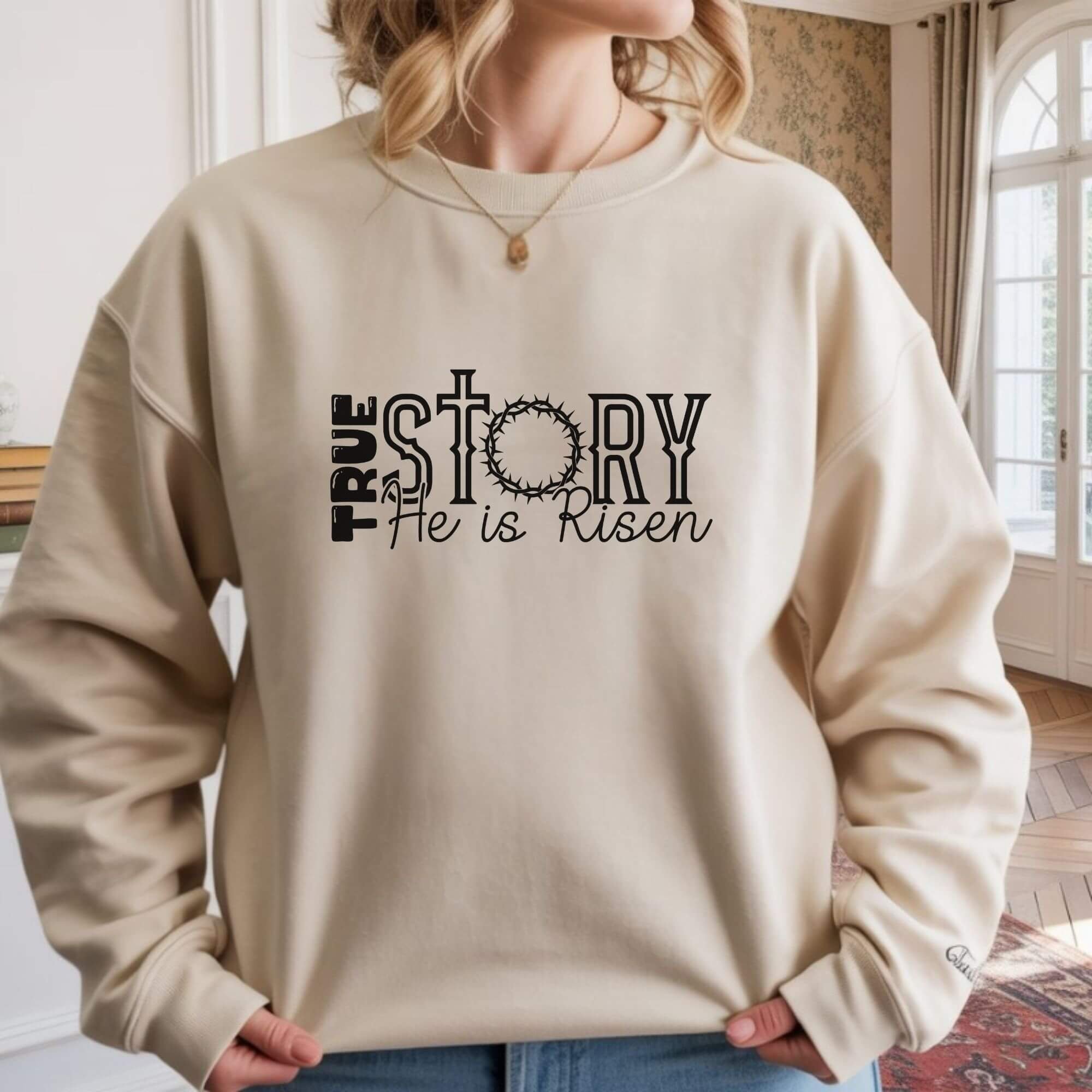 Cream Gildan sweatshirt with the Christian message “True Story He is Risen,” featuring a cross and crown of thorns design, laid flat on a bed with soft natural lighting.