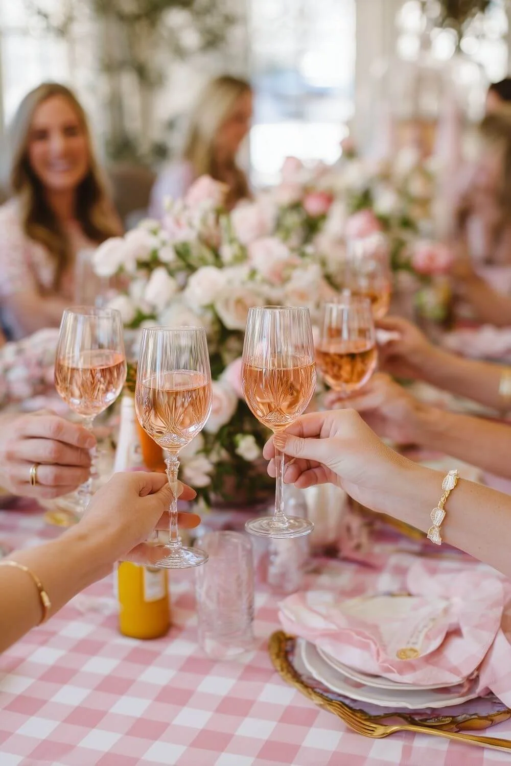 Friends raising glasses of rosé for a toast at a pink-themed Mother’s Day brunch table with floral centerpieces and elegant place settings.