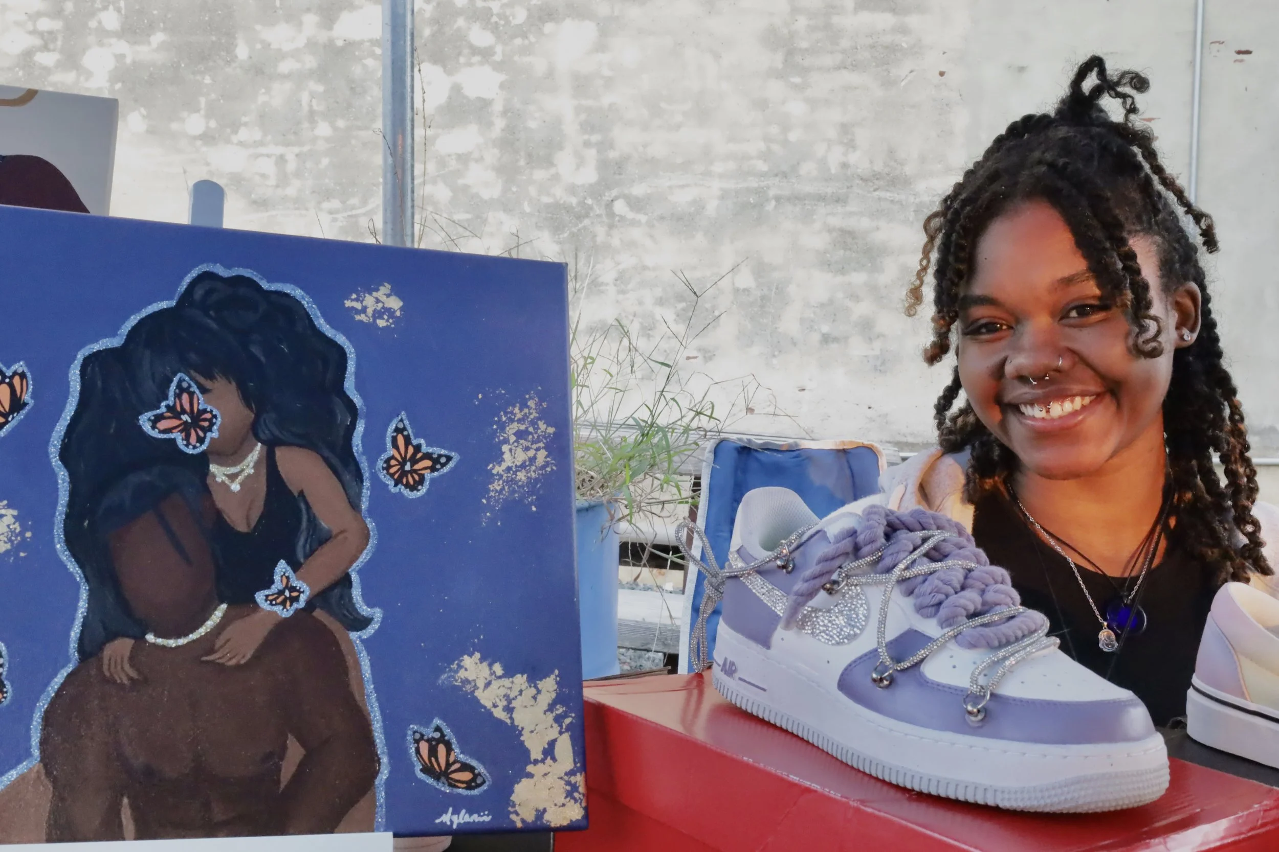 Smiling woman next to a painting of a couple with butterflies and a customized sneaker.
