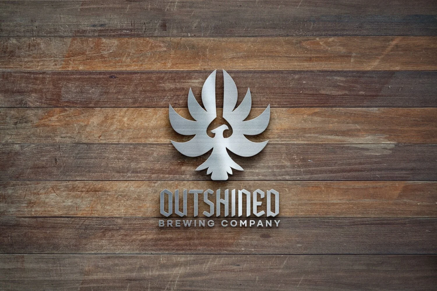 Metal sign of a stylized bird above the words 'OUTSHINED Brewing Company' on a wooden wall.