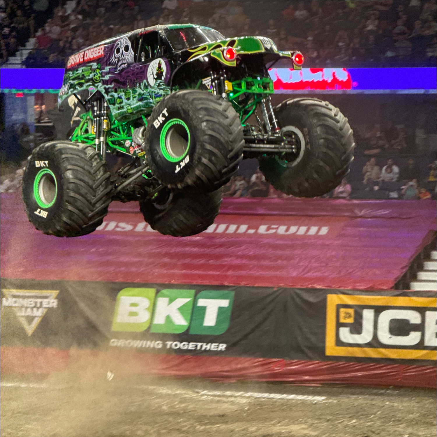 Green and black monster truck jumping over the arena floor