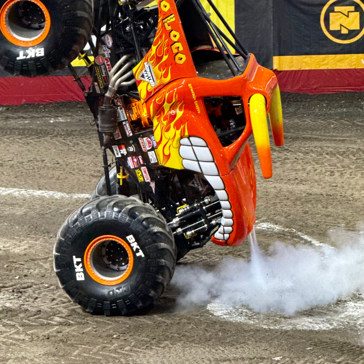 Orange monster truck balancing on two wheels amid smoke