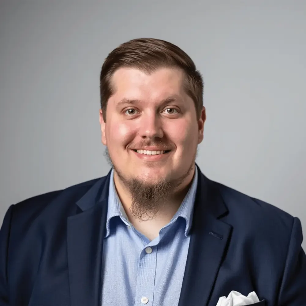 Parker Lee smiling in a navy blazer against a gray background